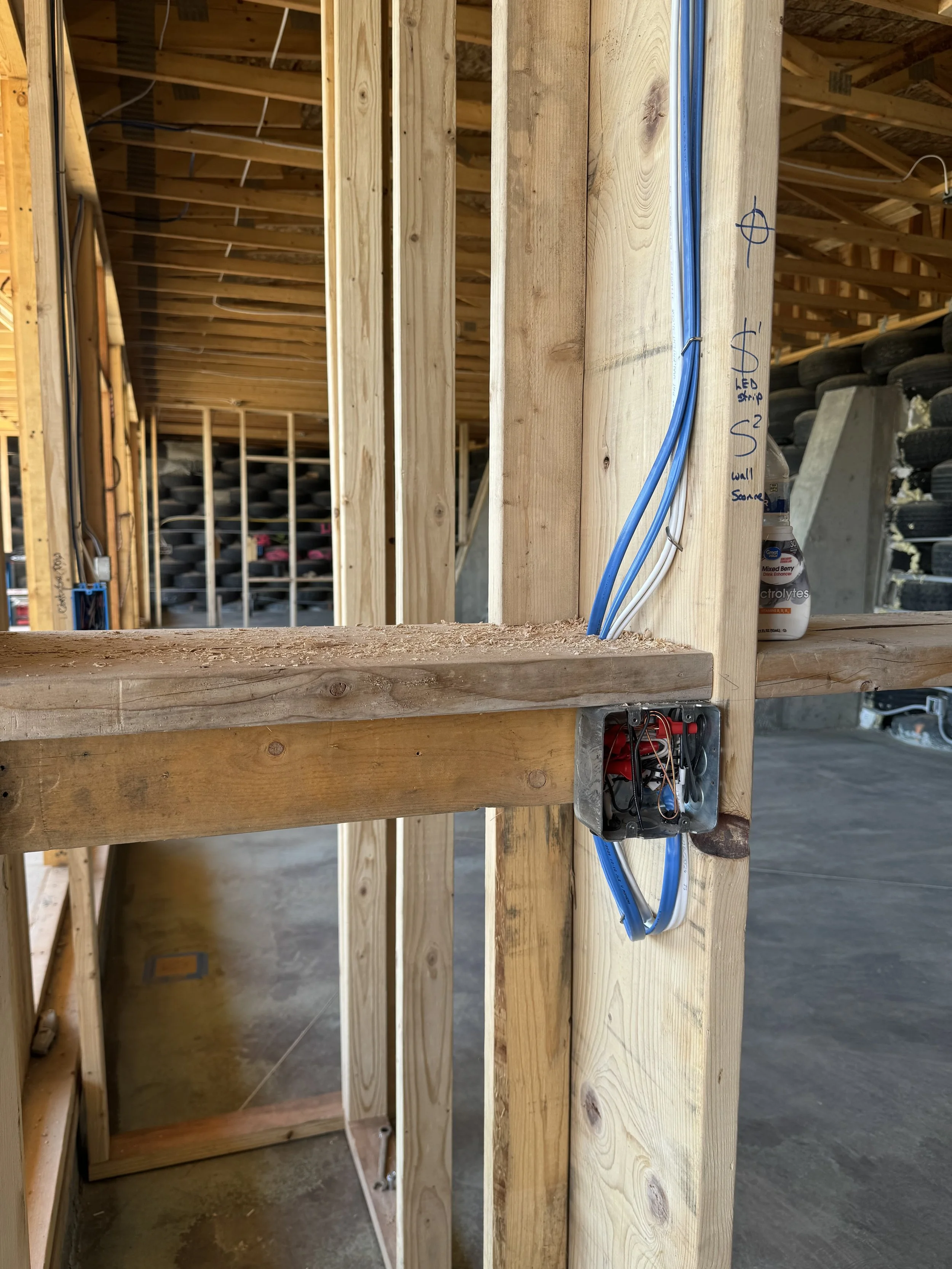 Construction site with electrical wiring installed in wooden framing, with notes and measurements written on the wood.