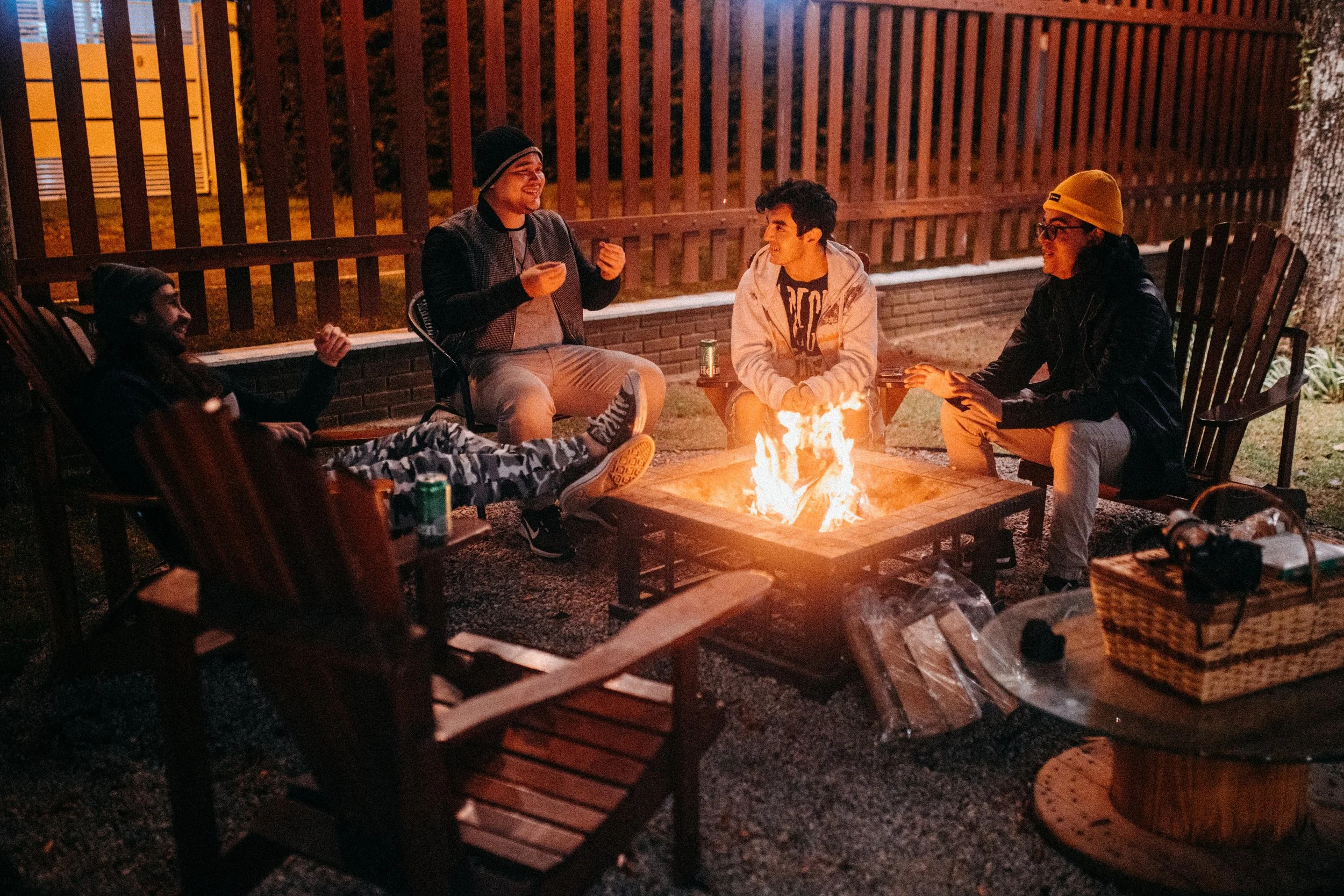 A group of friends sitting around a fire pit outside at night, enjoying conversation and laughter.