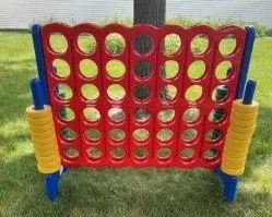 A giant Connect Four game outdoors on grass with a red frame and yellow and blue pieces.