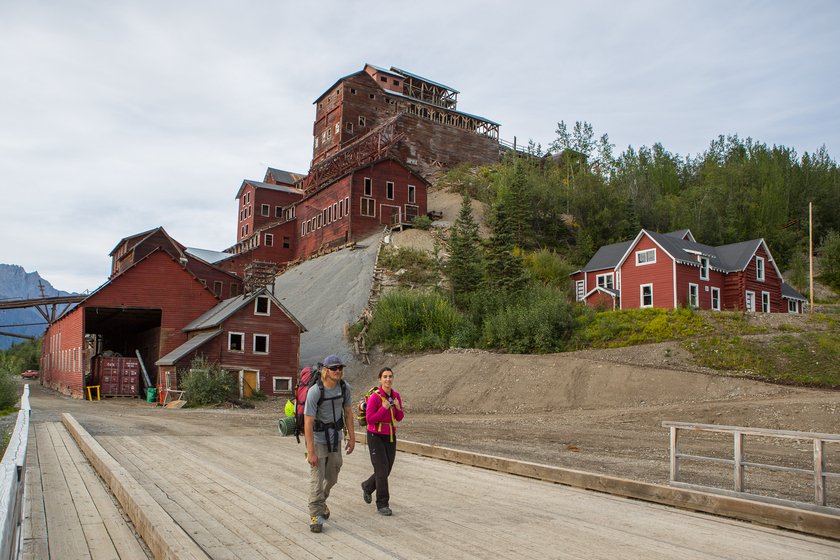 Hikers on bridge below Kennicott Mines buildings near McCarthy—gateway to adventures from St. Elias Station.
