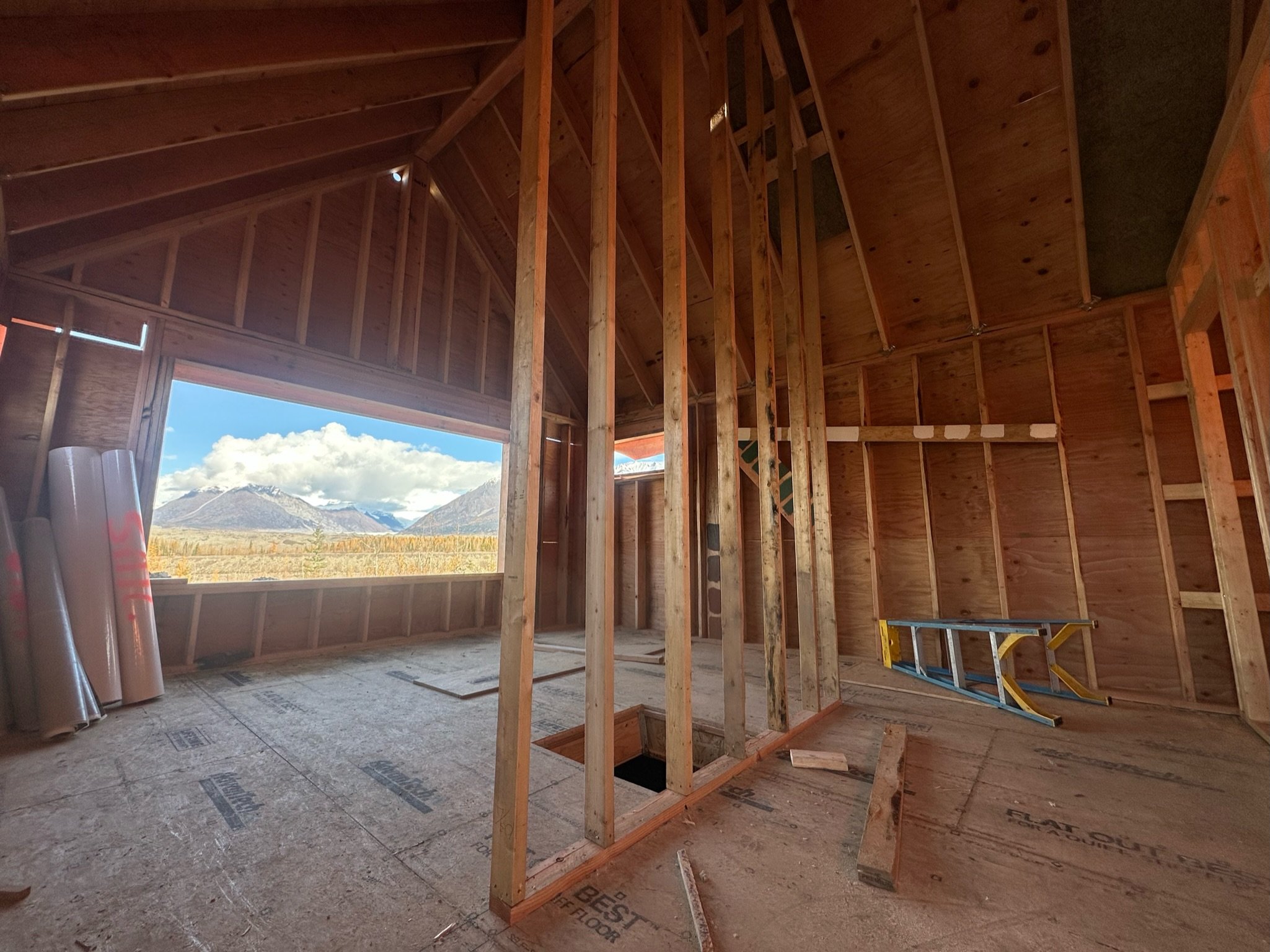 Interior view of a building under construction with exposed wooden framing and mountains visible through an open window