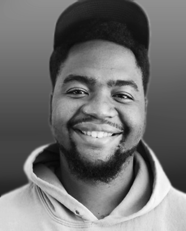 A young man smiling wearing a baseball cap and hoodie, in black and white.
