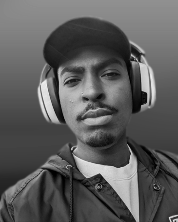 Close-up of a young man wearing headphones and a cap, looking at the camera in black and white.