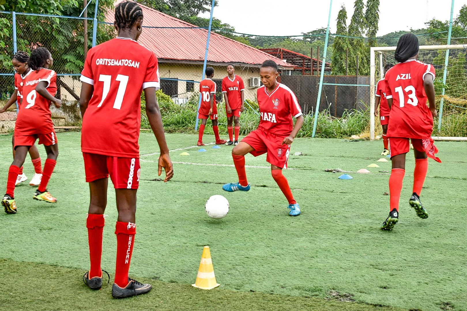 Youth black football athletes training on astroturf around cones and executing drills