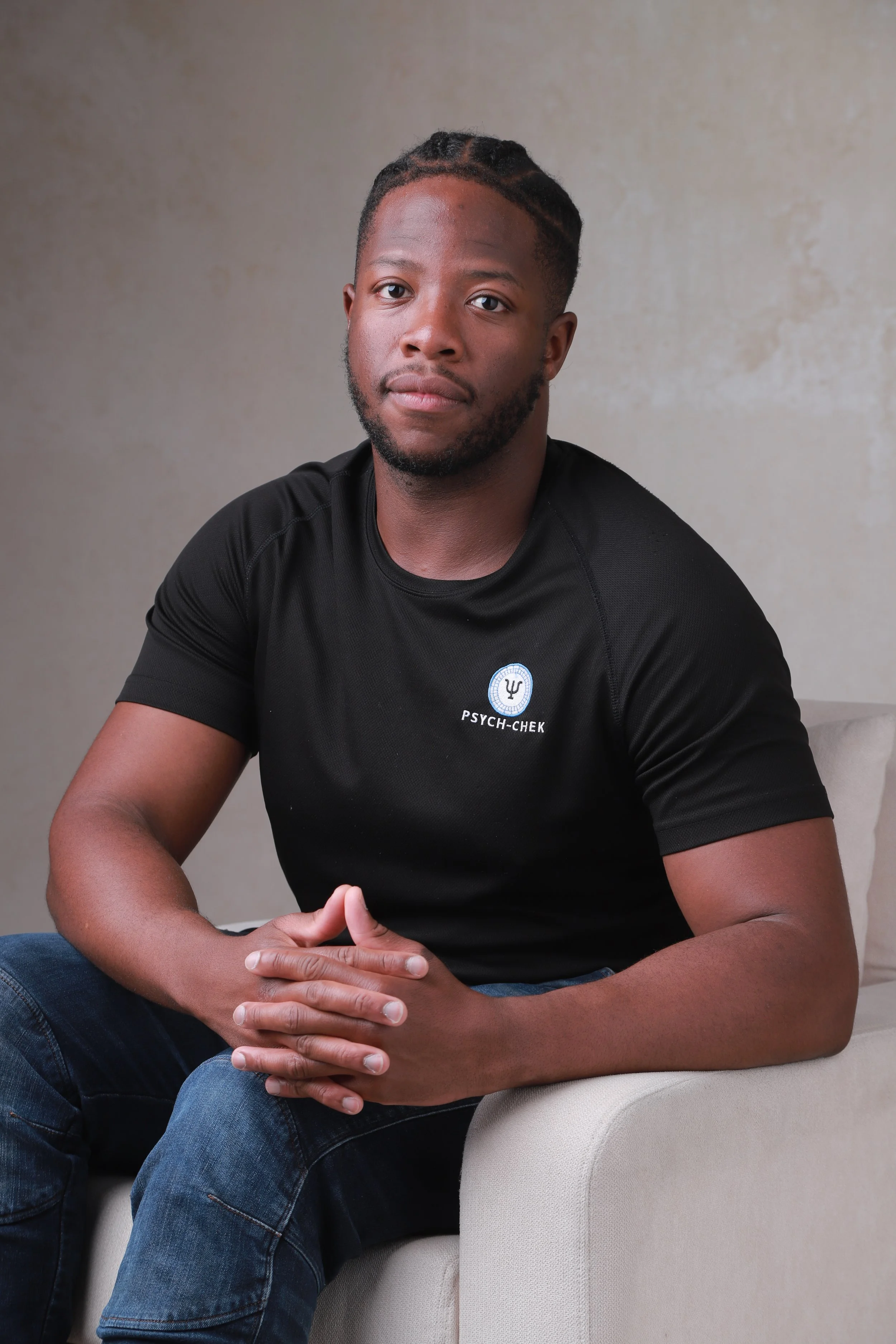 Black man (performance psychologist) sitting with his fingers interlocked looking at the camera