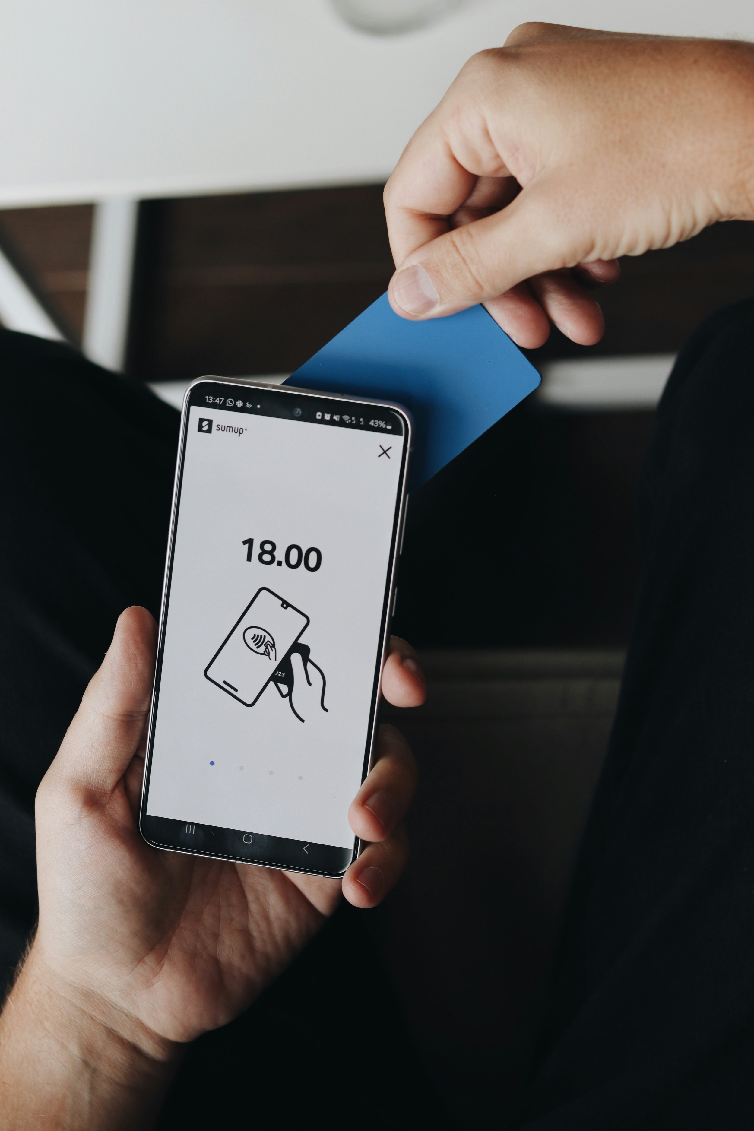Person holding a smartphone with a mobile payment app open, scanning a blue card at a point of sale device.