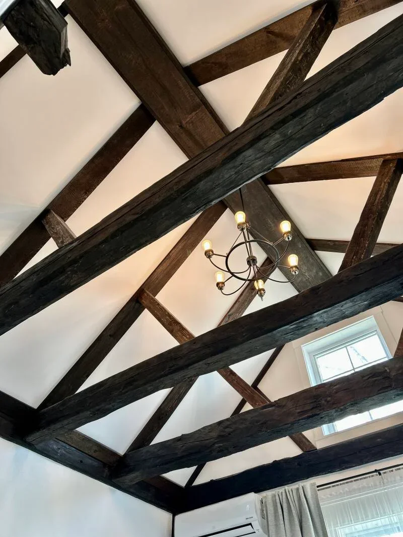 Ceiling with wooden beams, a chandelier with candles, a window, and curtains.
