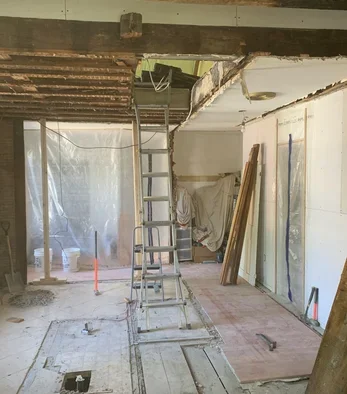 Construction site with a metal ladder, exposed beams, and construction materials in a partially renovated room.