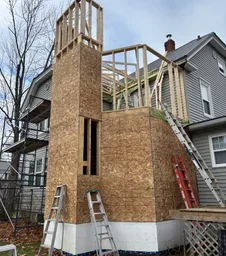 Construction of a wooden deck or extension on a residential house, with scaffolding and ladders present.