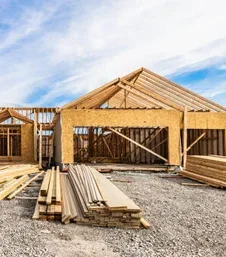 Wooden house under construction with building materials in front and blue sky