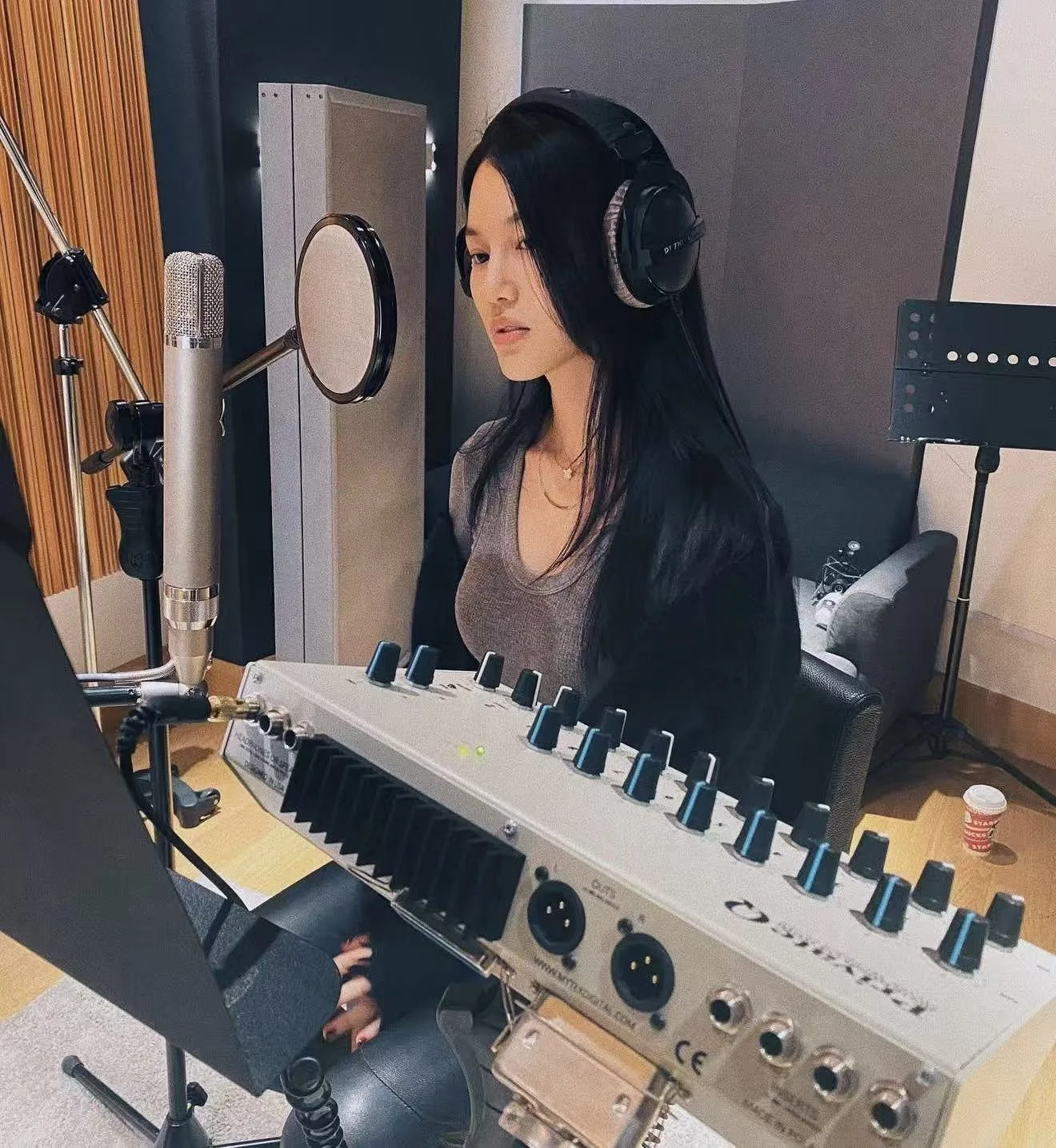 A woman recording vocals in a studio, wearing headphones, with professional audio equipment and a microphone in front of her.