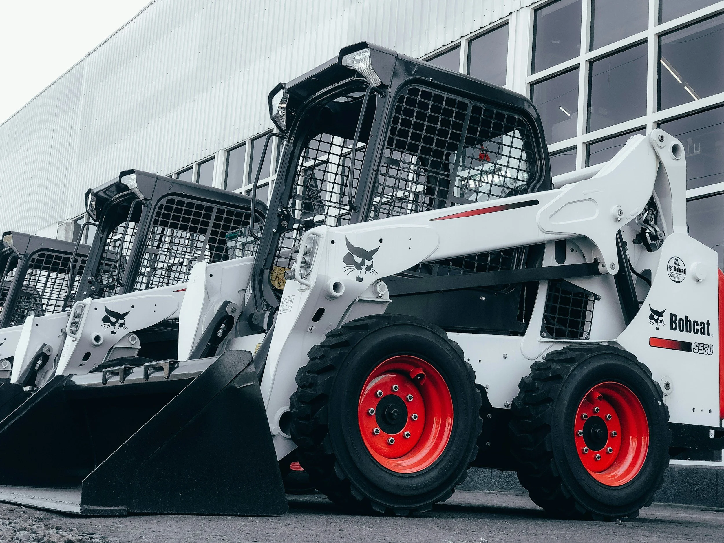 A white rental machine Bobcat skid-steer loader with black and red accents parked outside a building with large glass windows. Nassau Bahamas