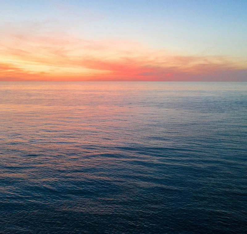 Calm ocean water at sunset with a colorful sky featuring shades of pink, orange, and blue.