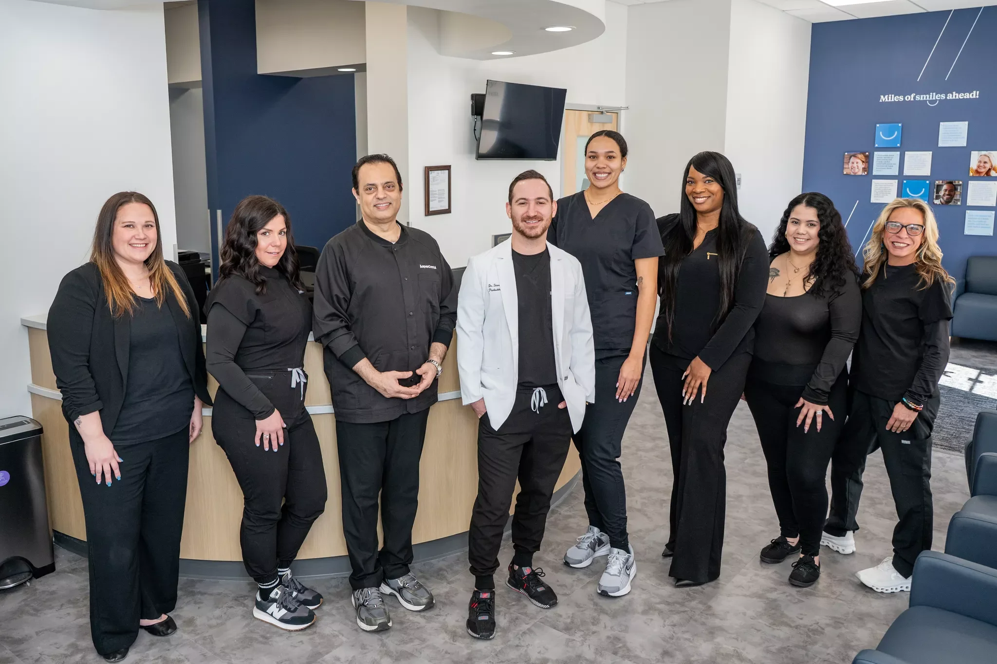 Group photo of nine healthcare professionals, including doctors and nurses, standing together in a modern medical office or clinic, smiling at the camera.