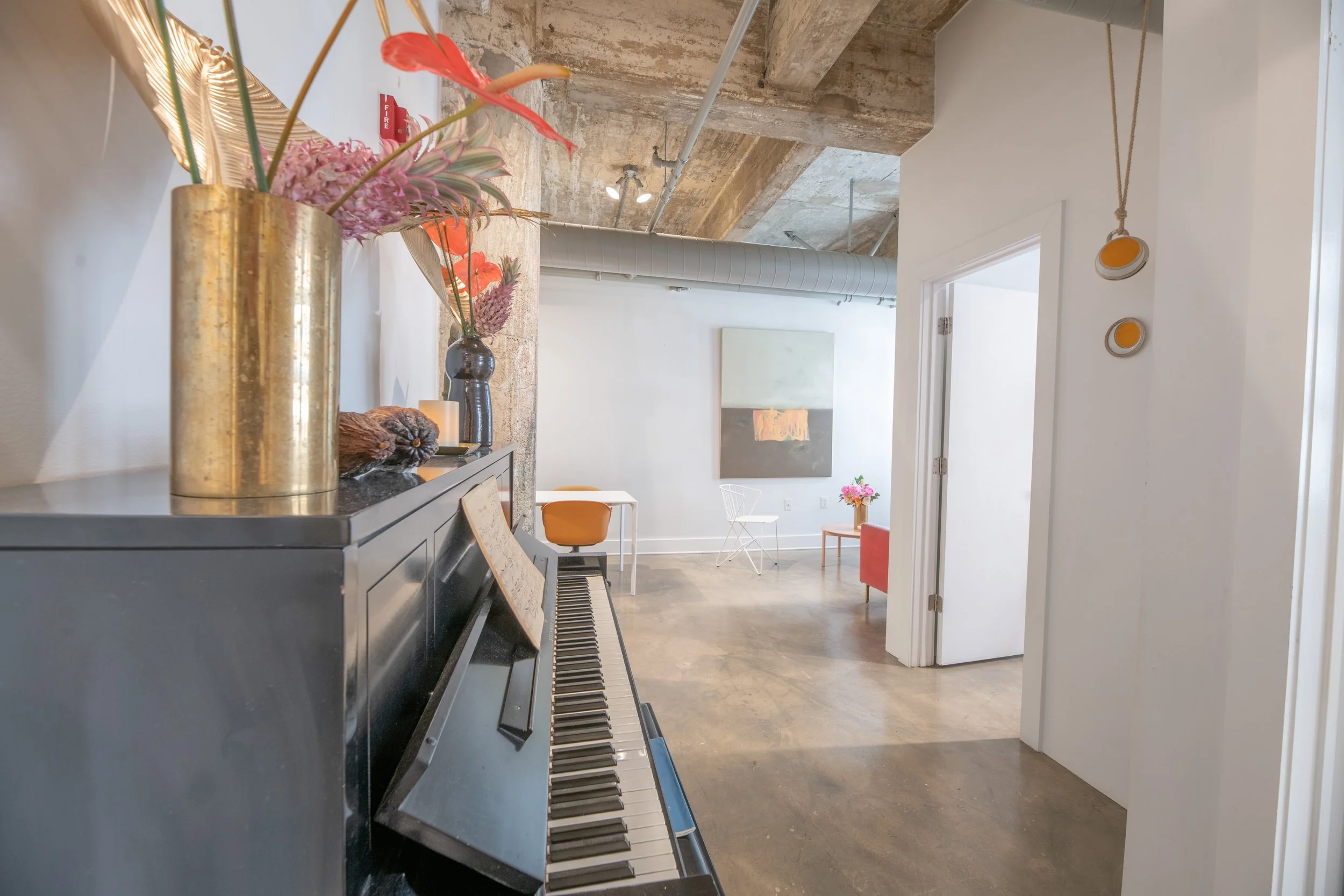 Interior of a modern living space with a black upright piano, floral arrangements, and artwork on the walls.