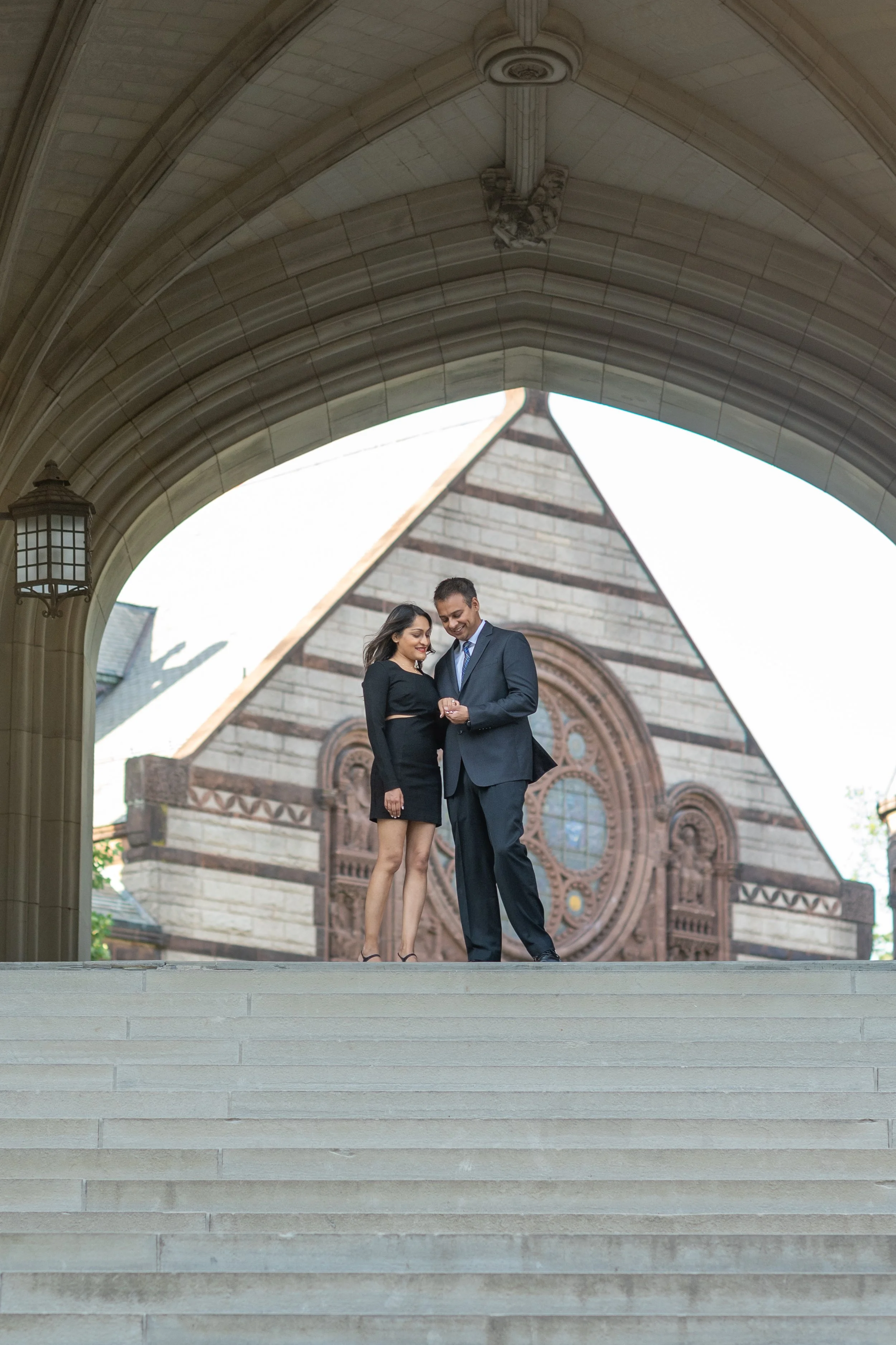 A couple in wedding attire standing on steps outside a church, with the church's arched entrance in the background.