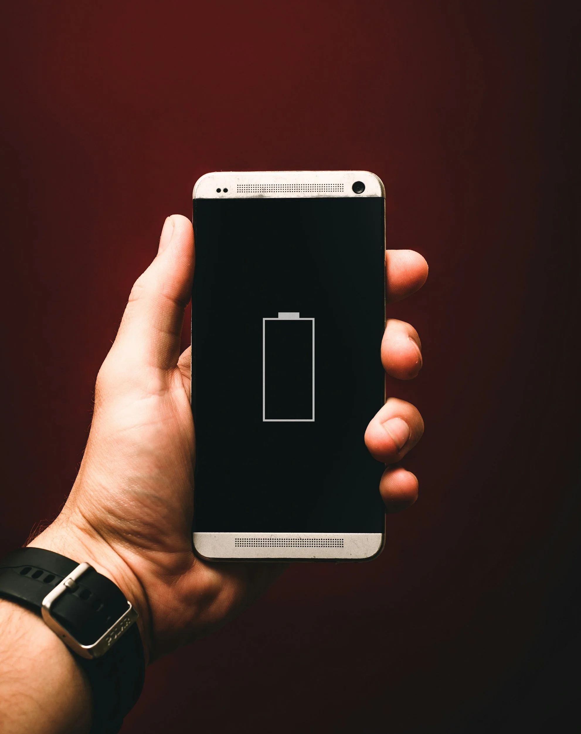Hand holding a smartphone with a battery charging icon on the screen.