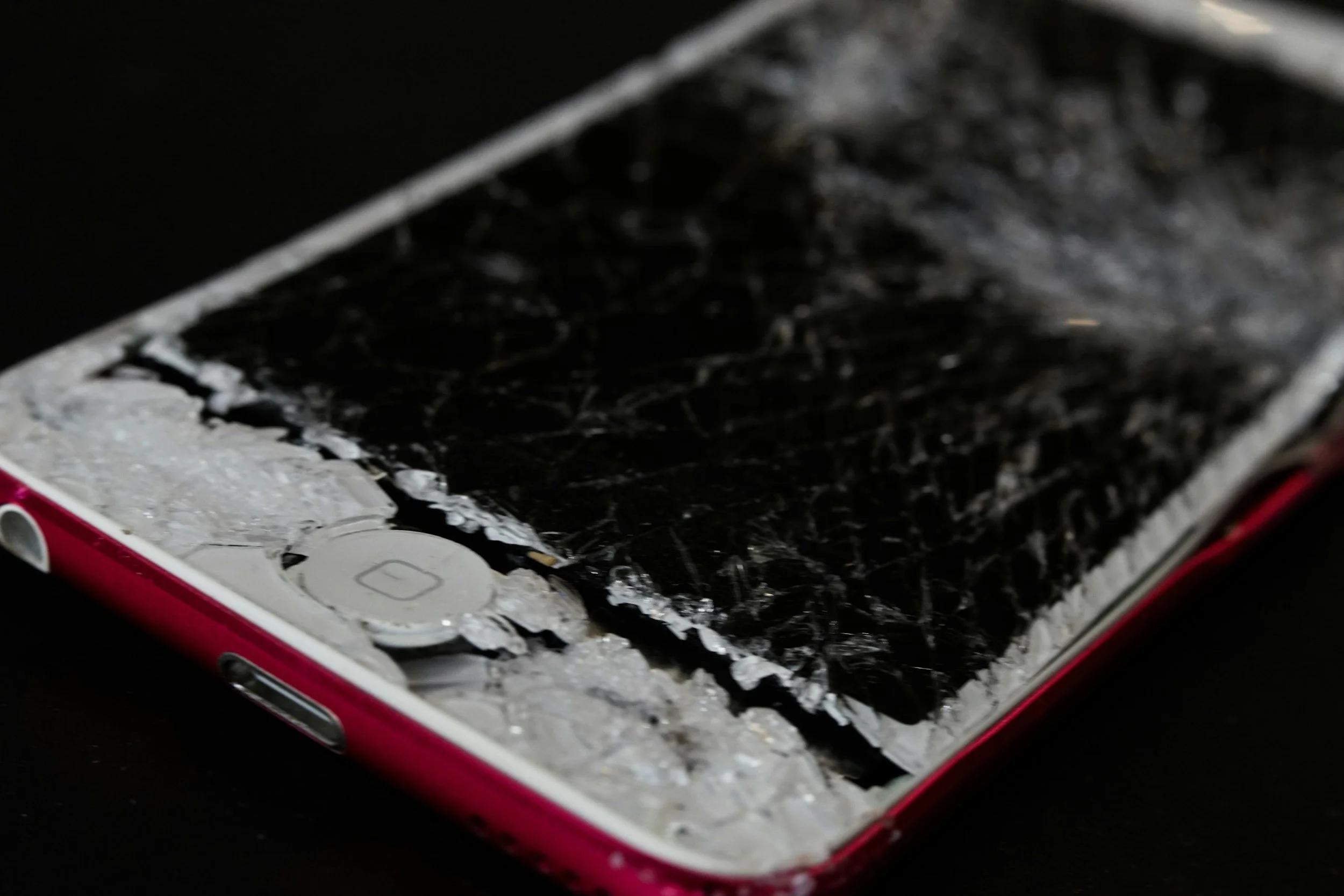 Close-up of a damaged smartphone with a shattered black screen and icy frost around the edges.