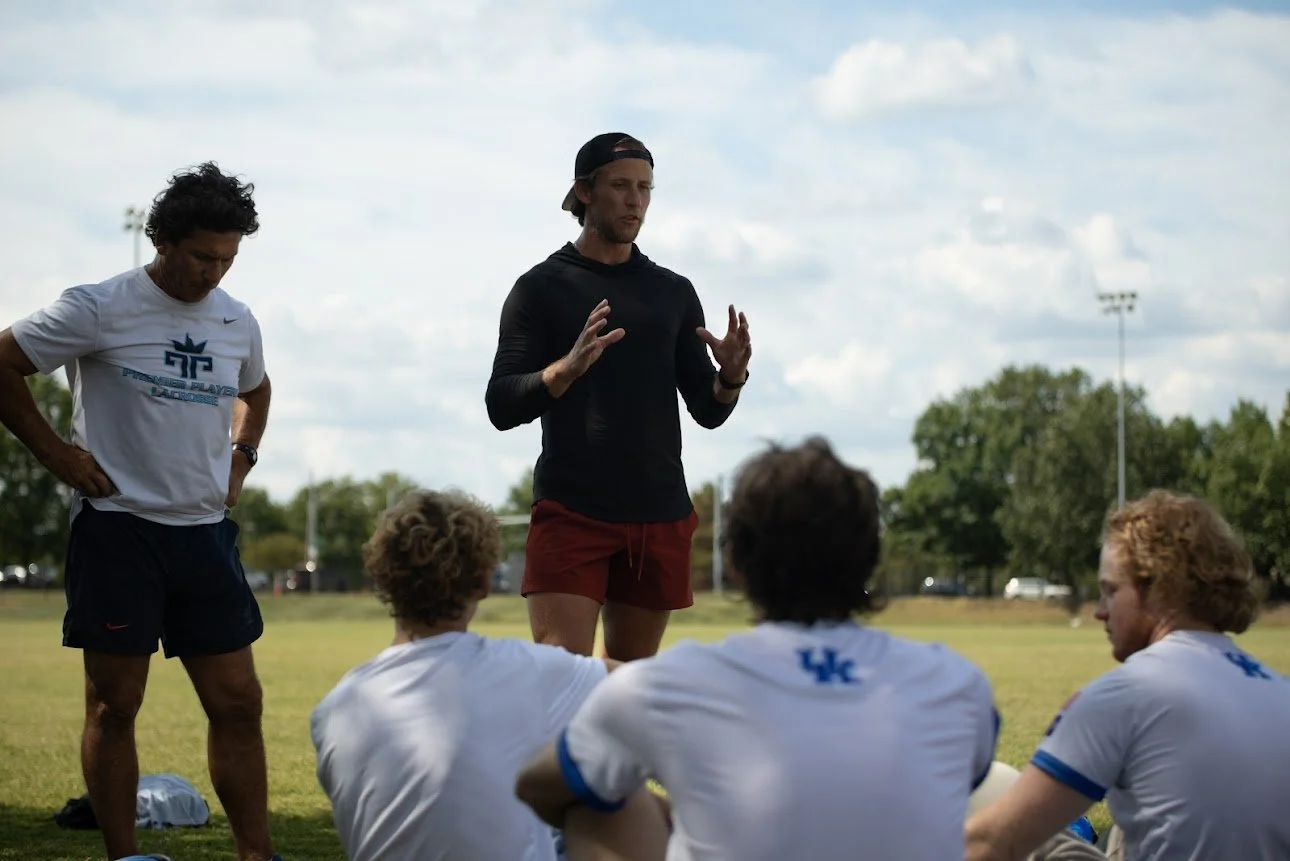 A coach giving instructions to a football team during practice on a grassy field.