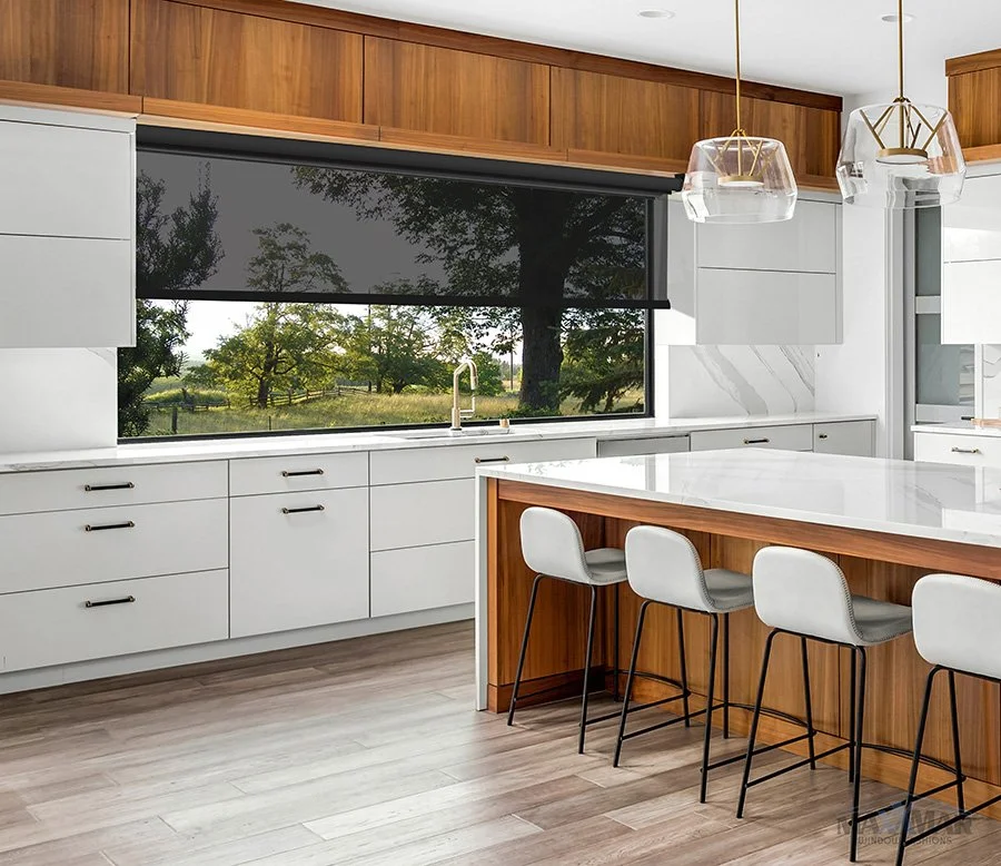 Modern kitchen with white cabinets, a large window with a view of trees and a grassy field, a white marble island with four bar stools, wooden accents, and contemporary pendant lights.