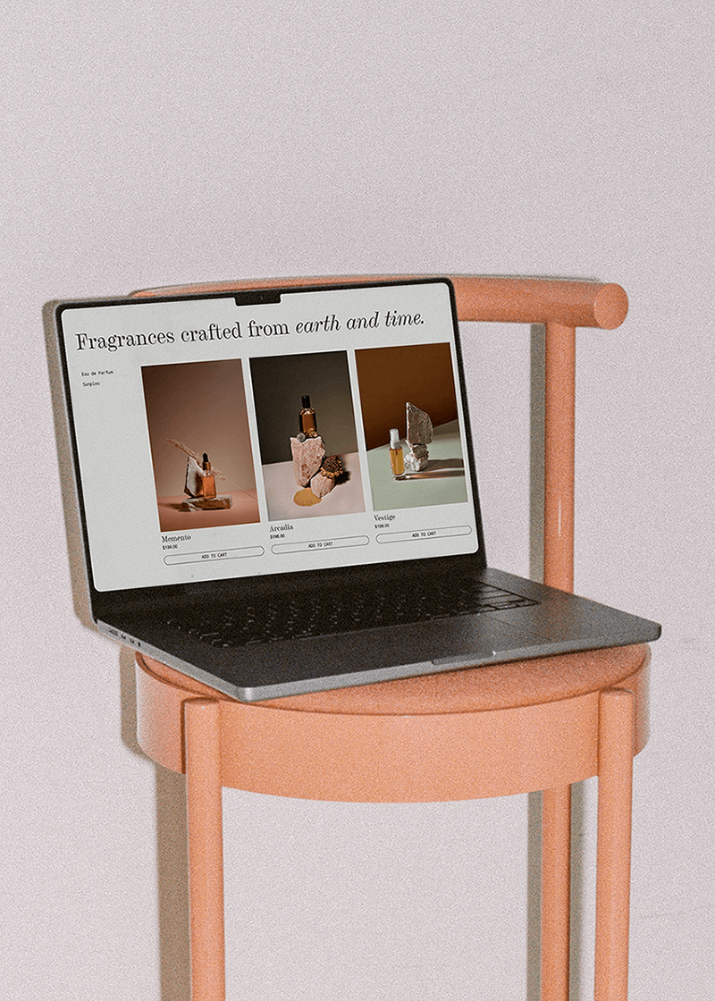 A laptop displaying an online store for fragrances, sitting on a pink chair against a plain wall.