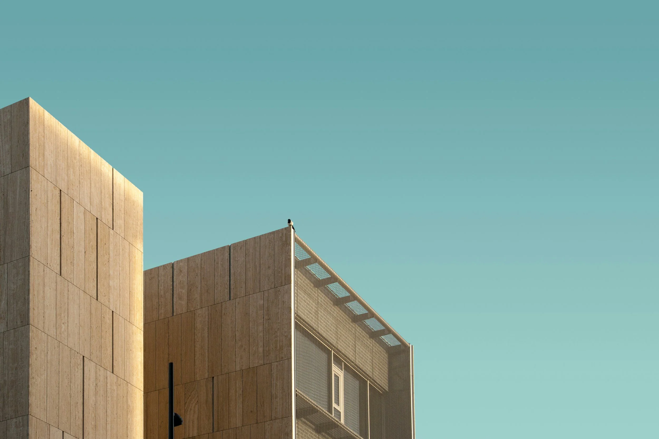 Close-up of a modern building with beige stone walls and a blue sky in the background.