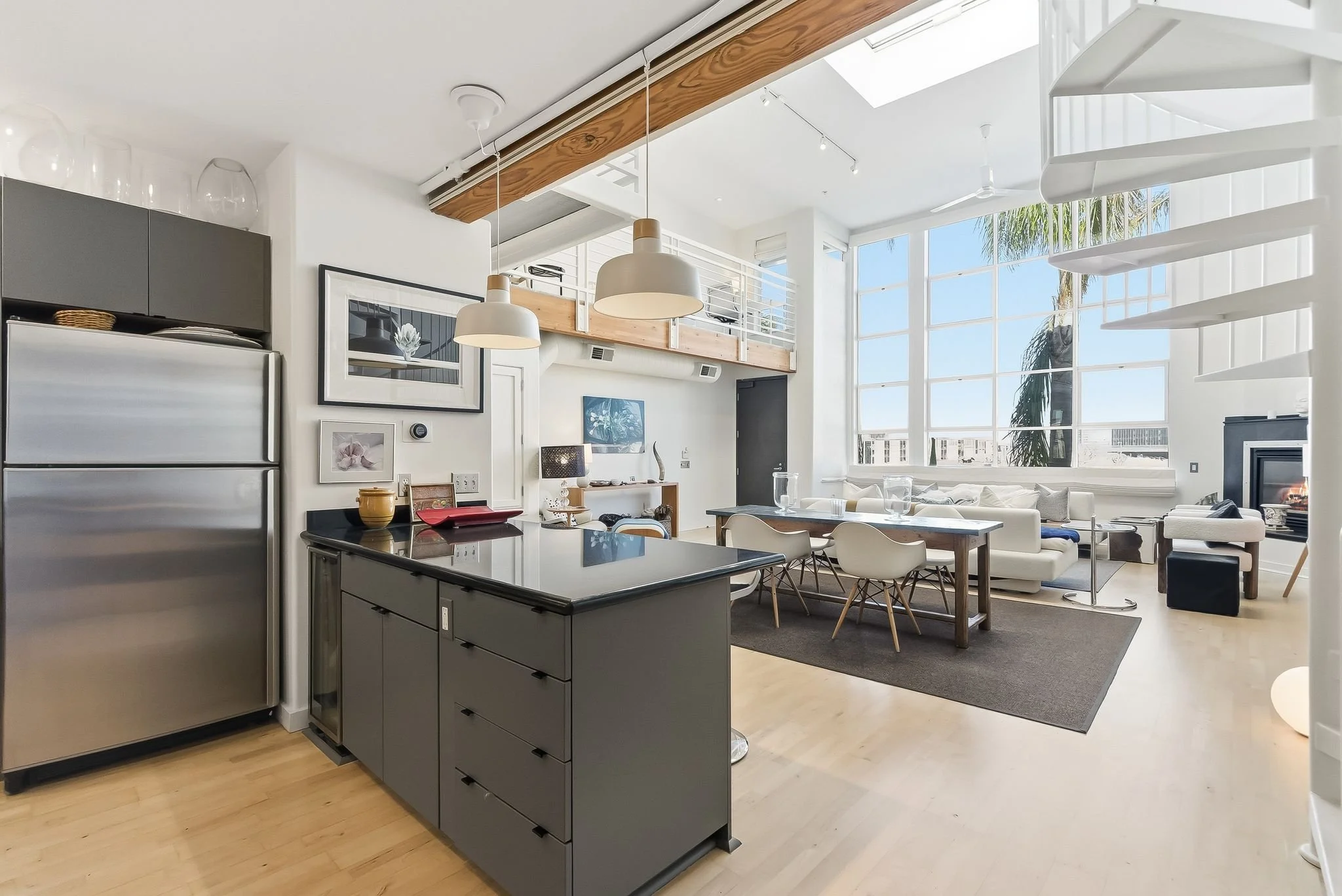 Open-concept living room and kitchen with large windows, modern furniture, and minimalist decor.