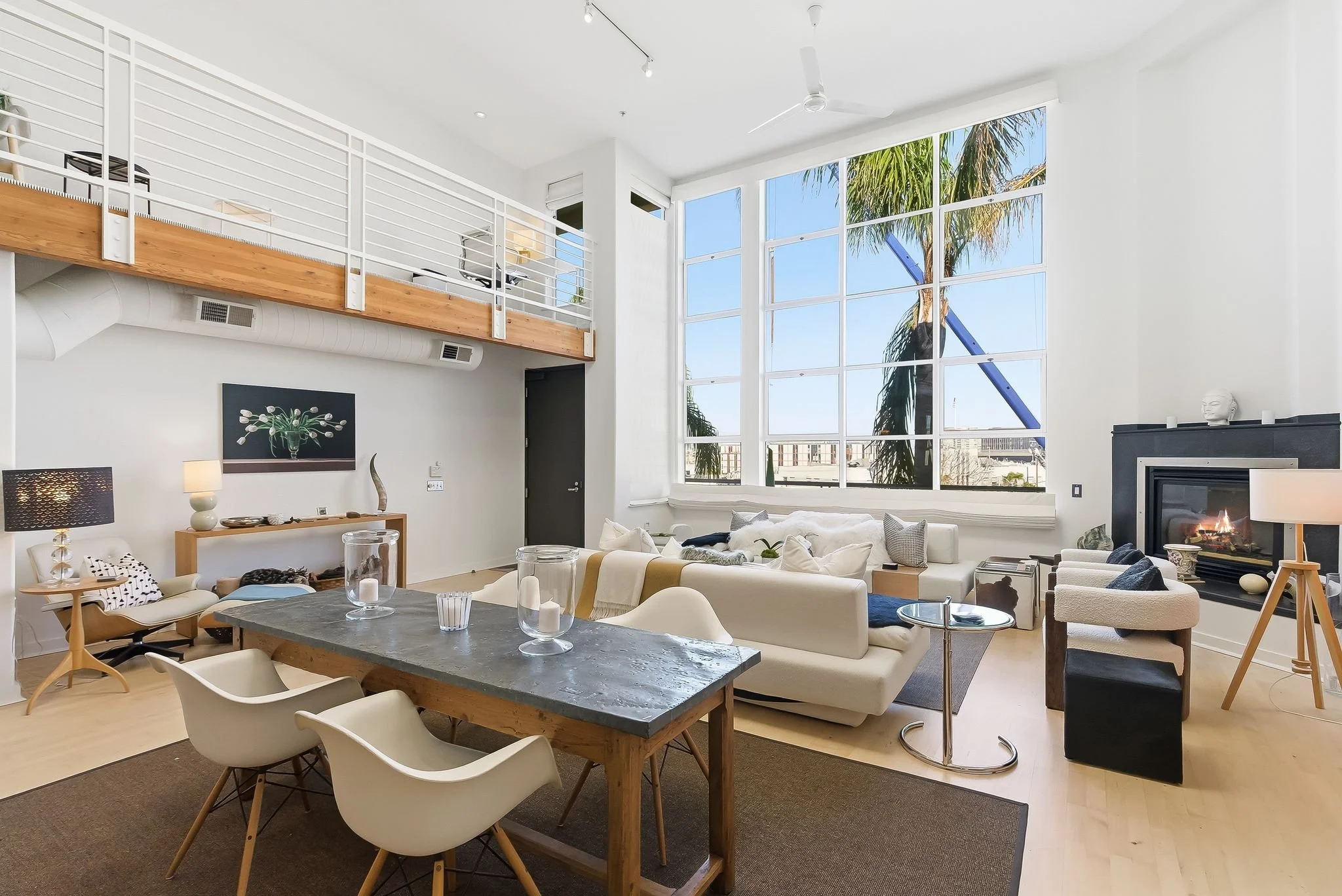 Bright living room with large windows, white walls, modern furniture, fireplace, and an open loft area.