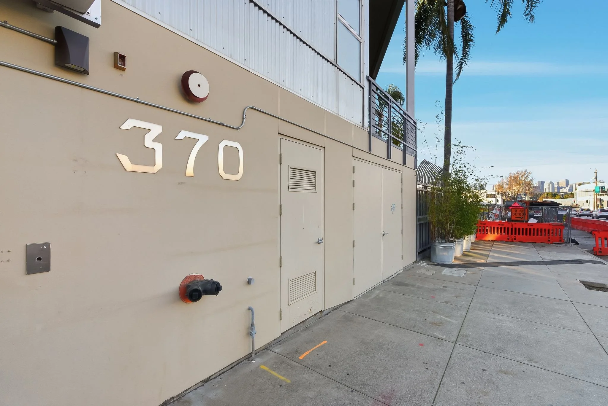 Building exterior with the number 370, fire hydrant, and sidewalk, with tall palm trees and city skyline in the background.
