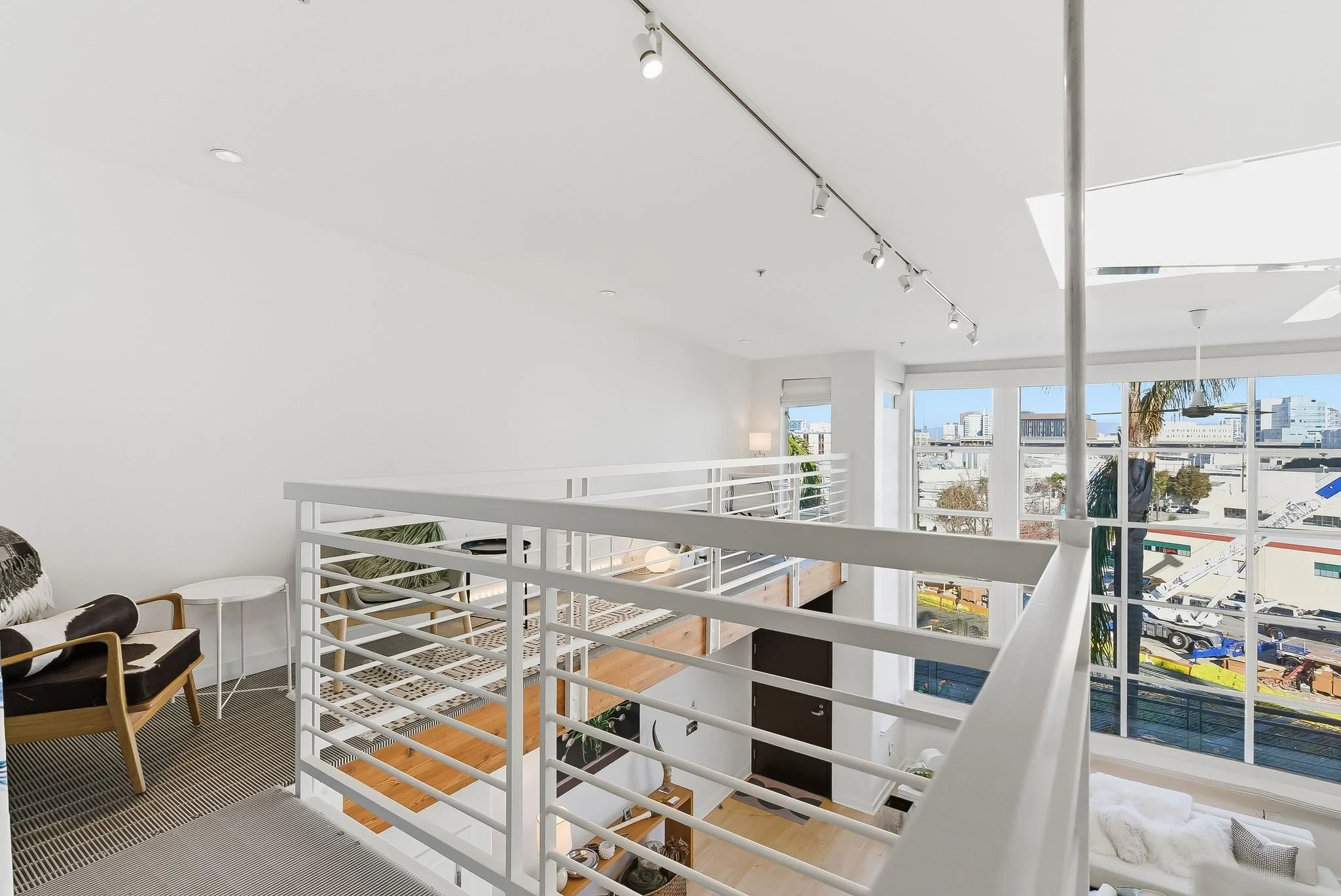 Modern indoor loft with white walls, large windows, and a white metal railing overlooking the lower level.