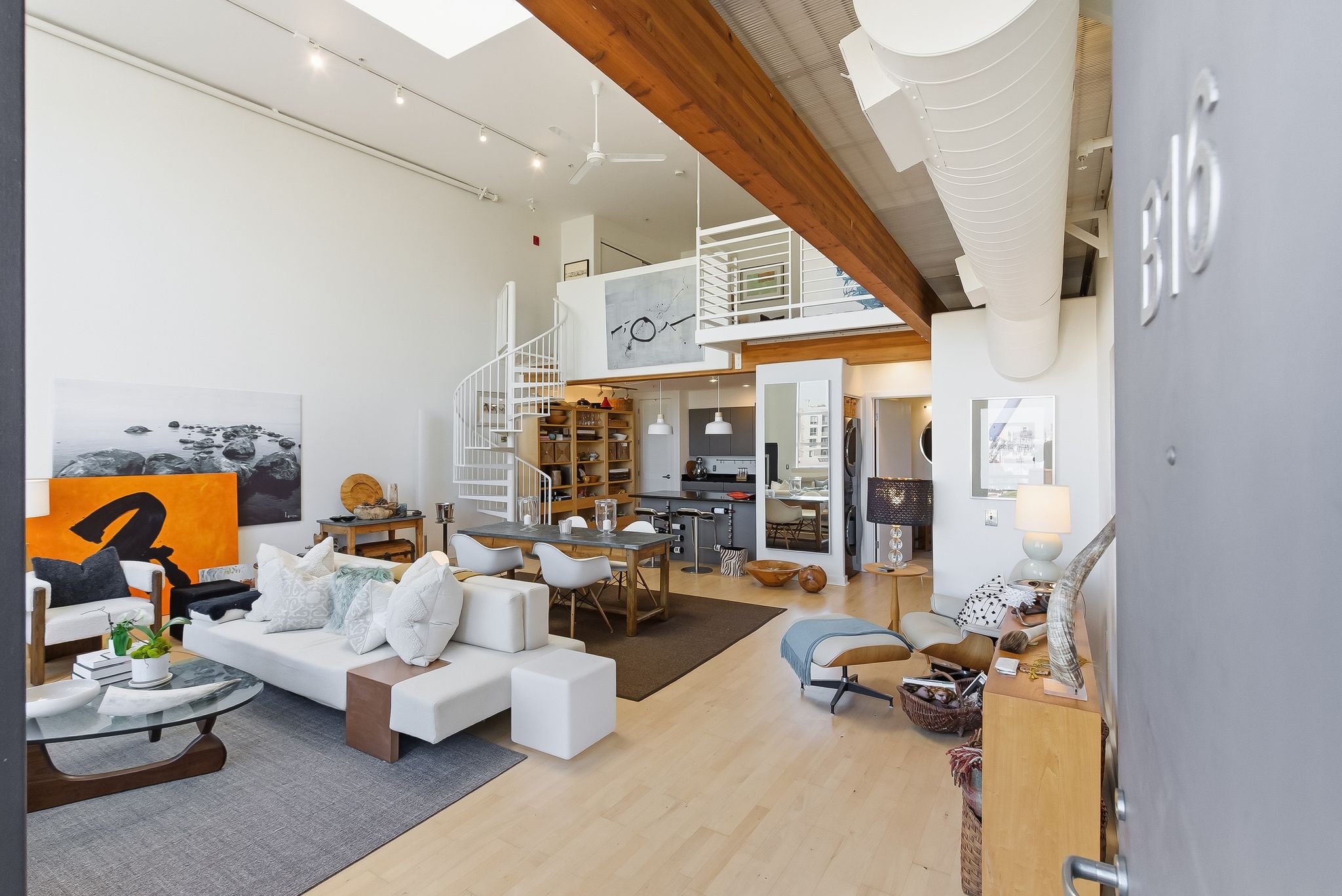 Interior of a modern, open-concept apartment with high ceilings, a spiral staircase, and a mix of contemporary and vintage decor.
