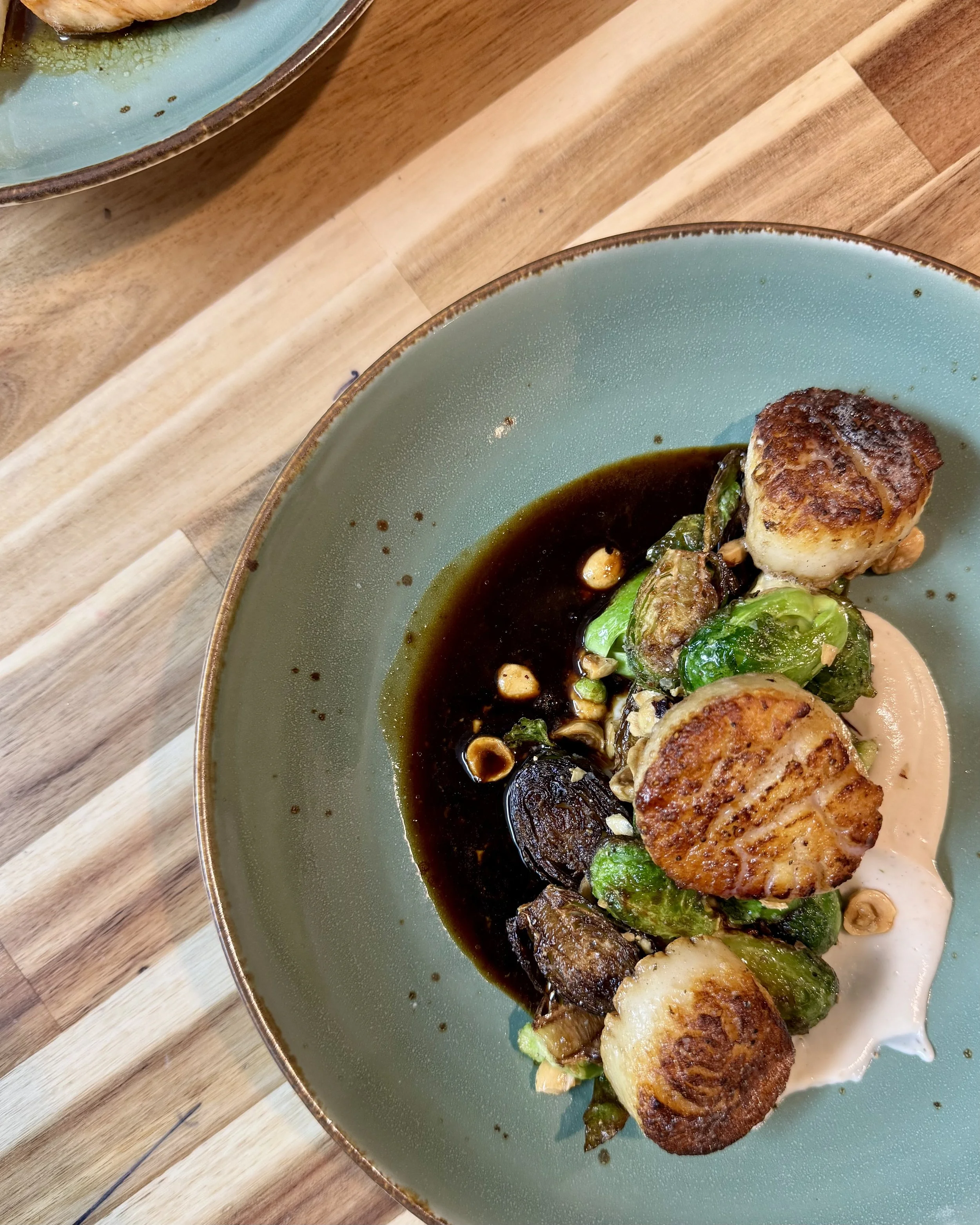 Seared scallops with Brussels sprouts, a dark sauce, and creamy dollop on a green plate.