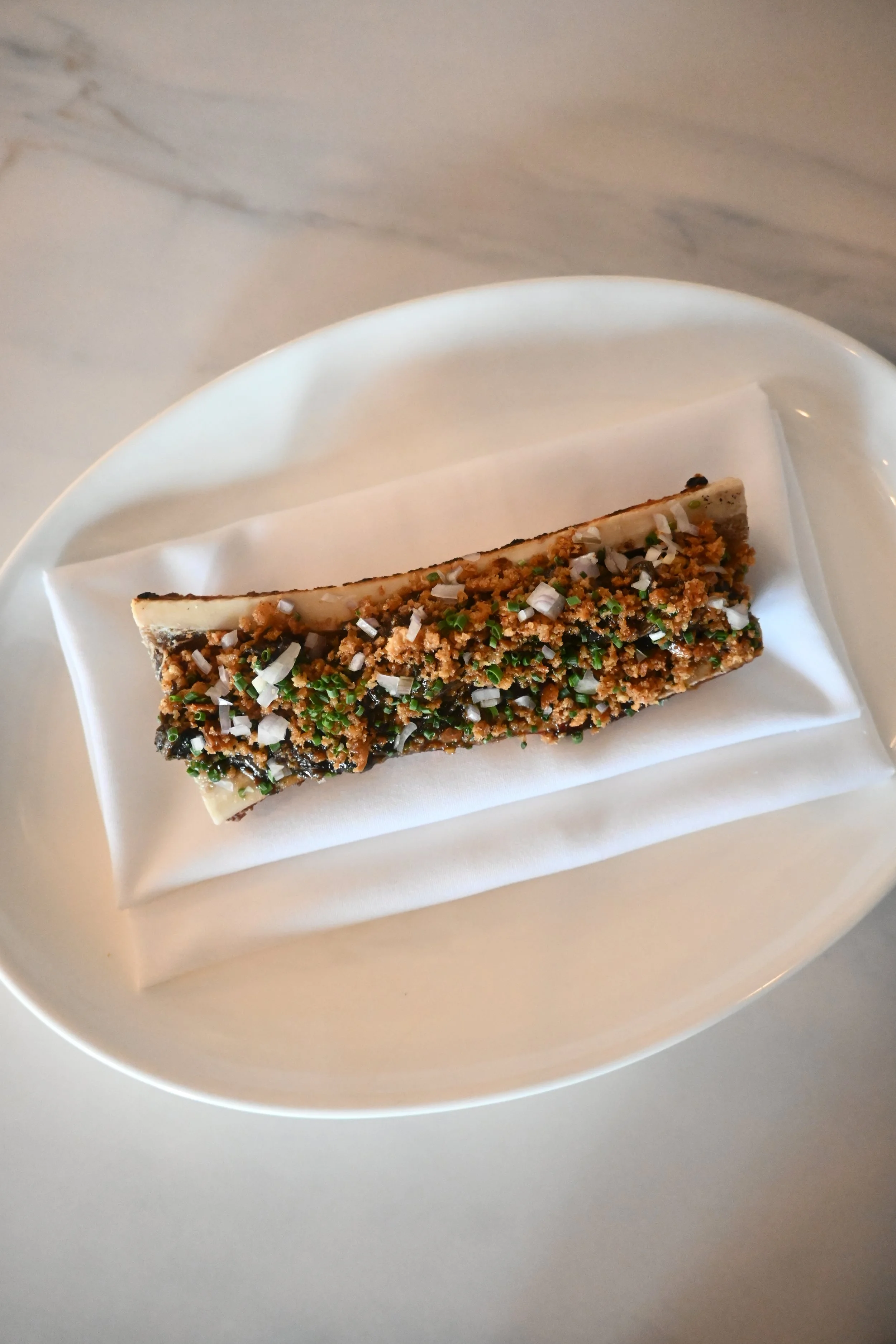 A crispy eel sushi roll topped with chopped green onions, sesame seeds, and crunchy breadcrumbs served on a white plate with a white napkin.