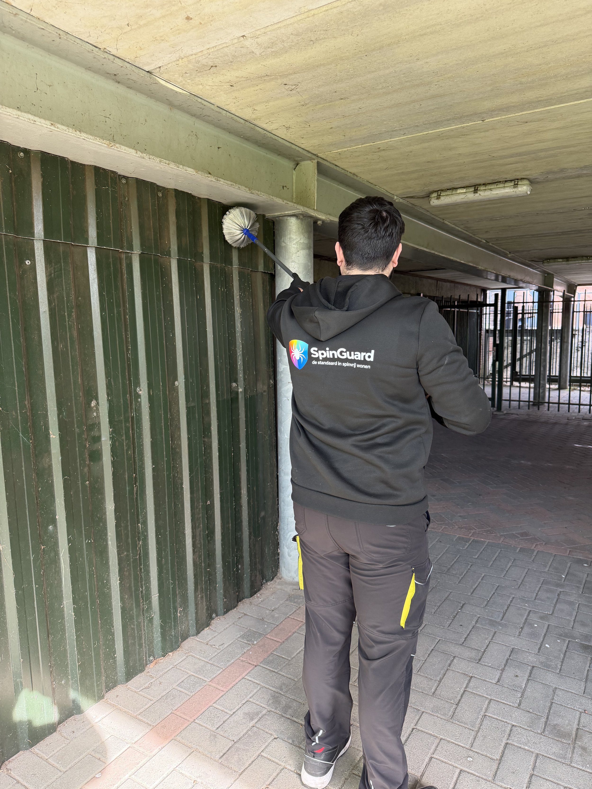 Persoon die een borstel gebruikt om vuil van een muur en plafond te vegen onder een brug of verlaagde structuur.