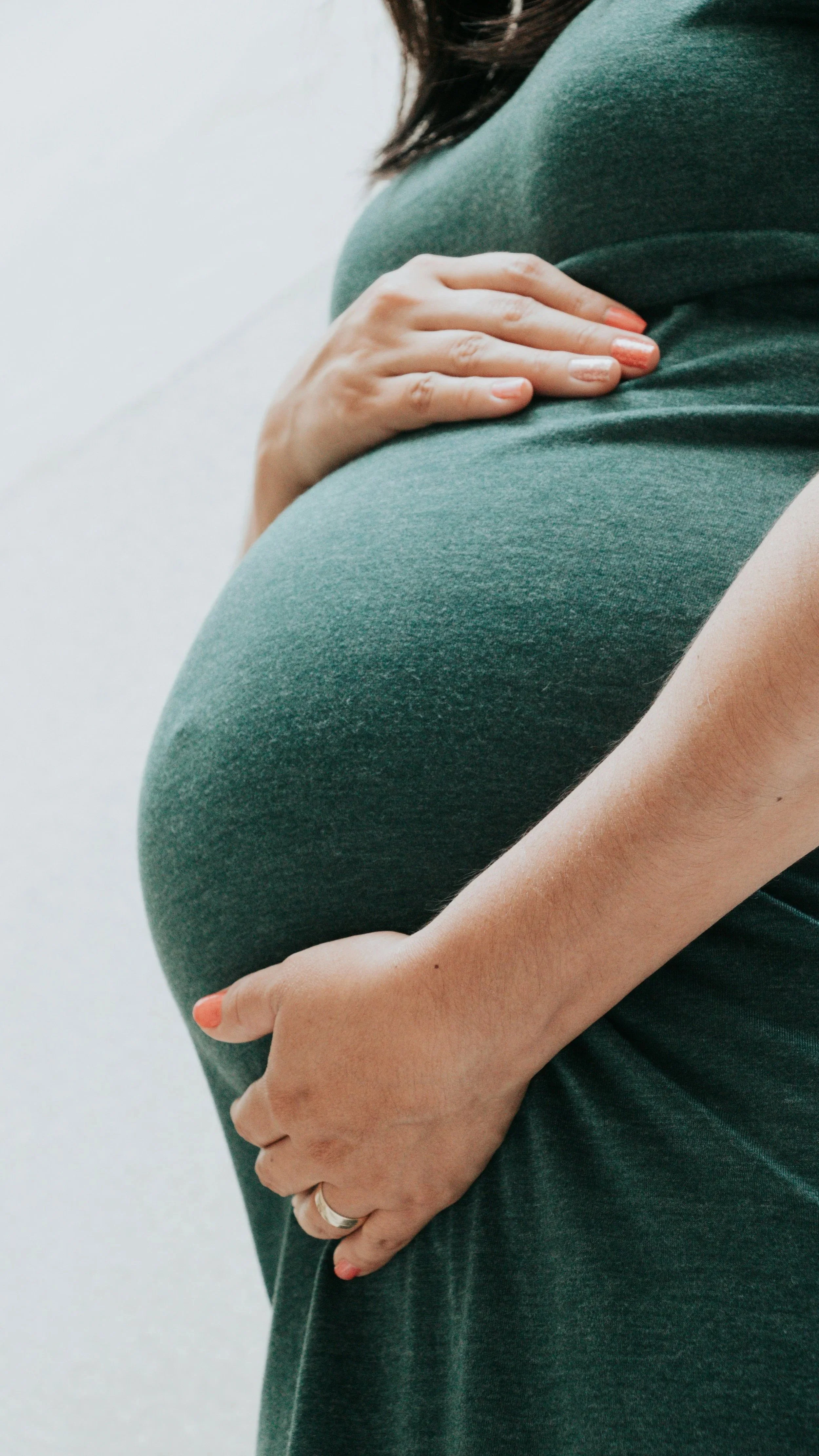 Close-up of a pregnant woman in a green top holding her belly with one hand, showing her pregnancy.