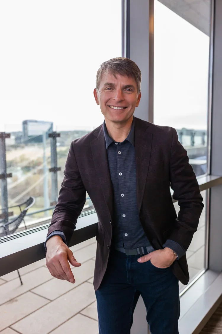 Jeremy Ramsey sales leader in a blazer and dark shirt standing next to a large window on a balcony or terrace.