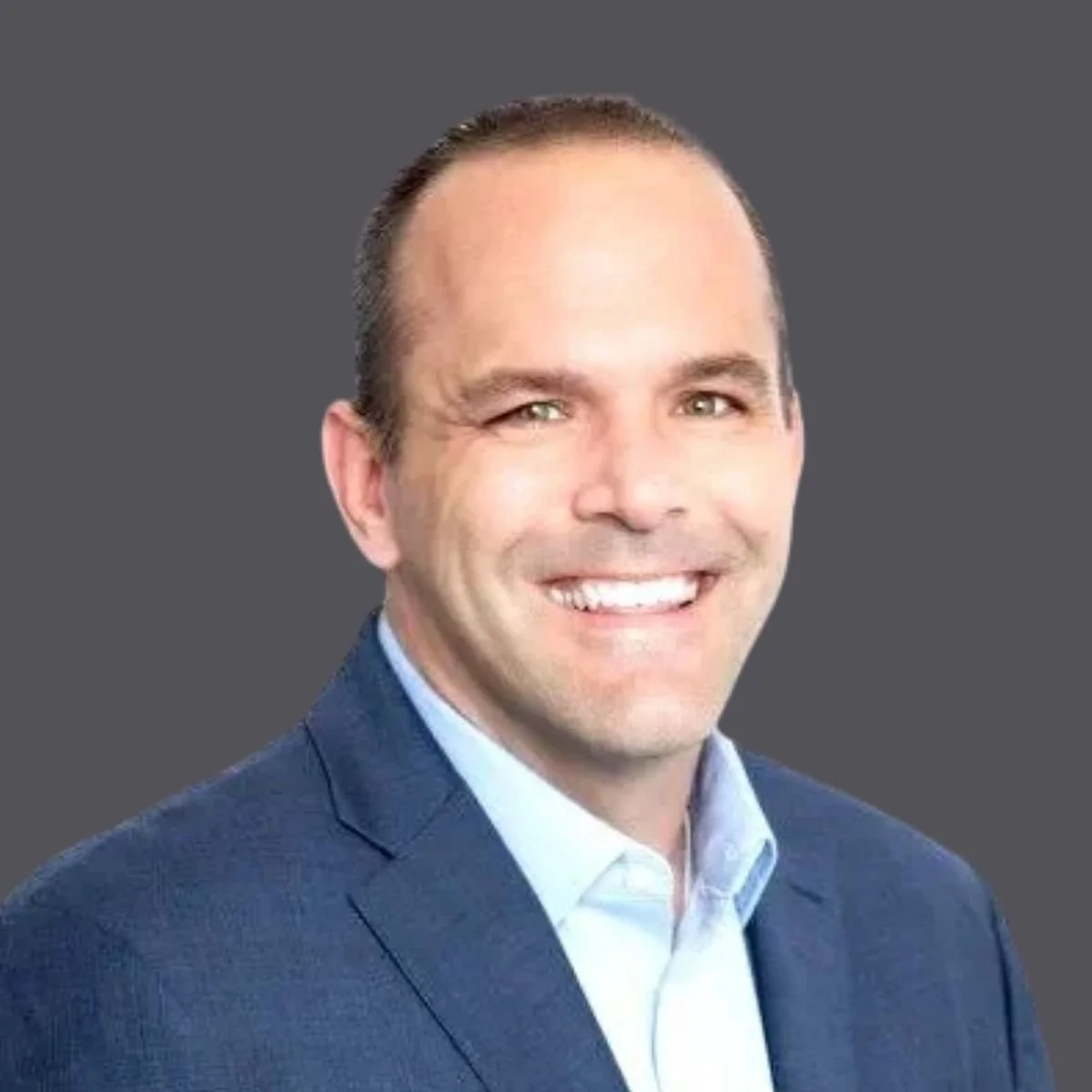 Headshot of a man in a suit smiling against a gray background.