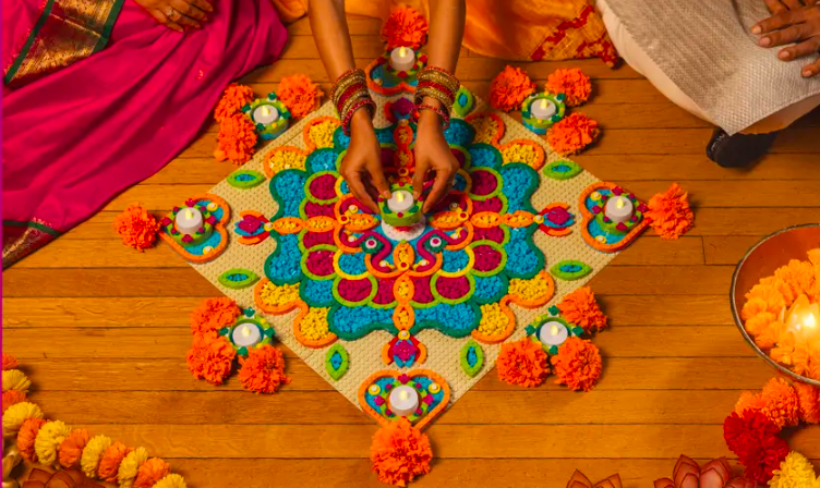 People creating a colorful rangoli design with candles, flowers, and intricate patterns on a wooden floor for a traditional celebration.