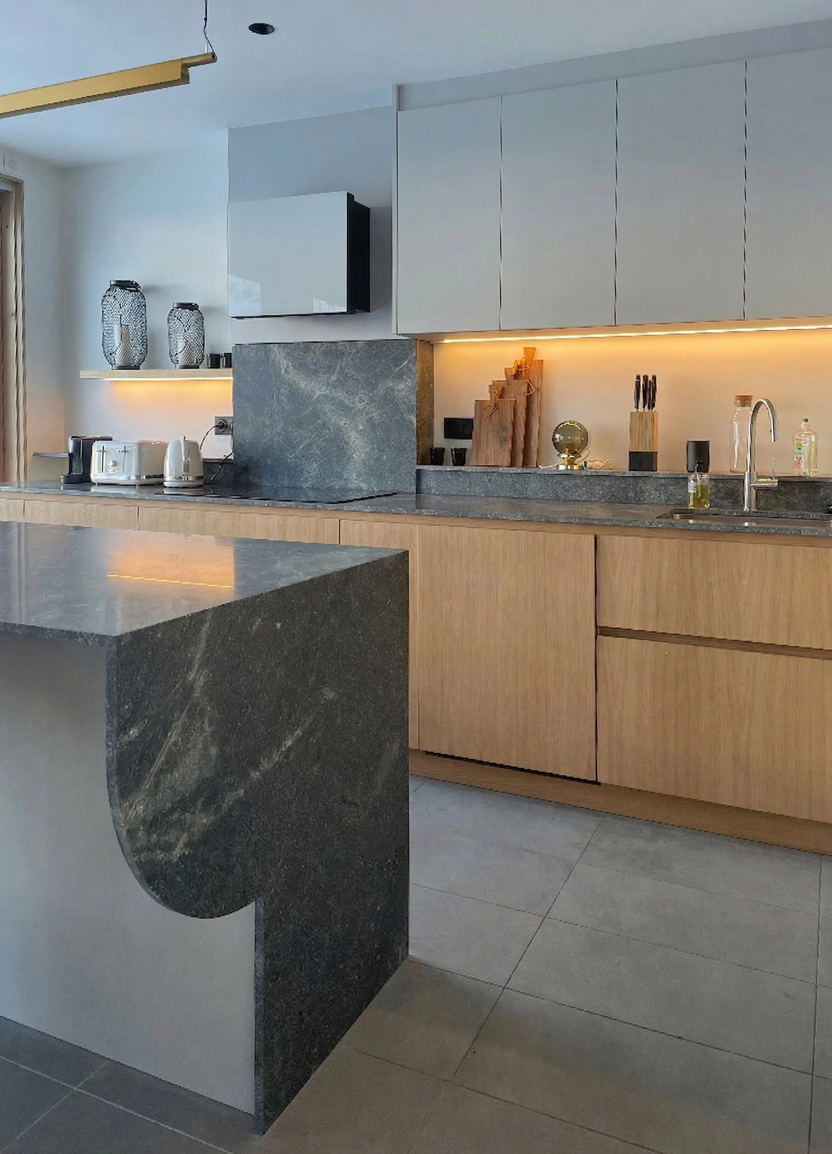 Cuisine moderne avec plan de travail en pierre aux lignes courbes et armoires en bois clair, accessoires de cuisine et décoration minimaliste.
