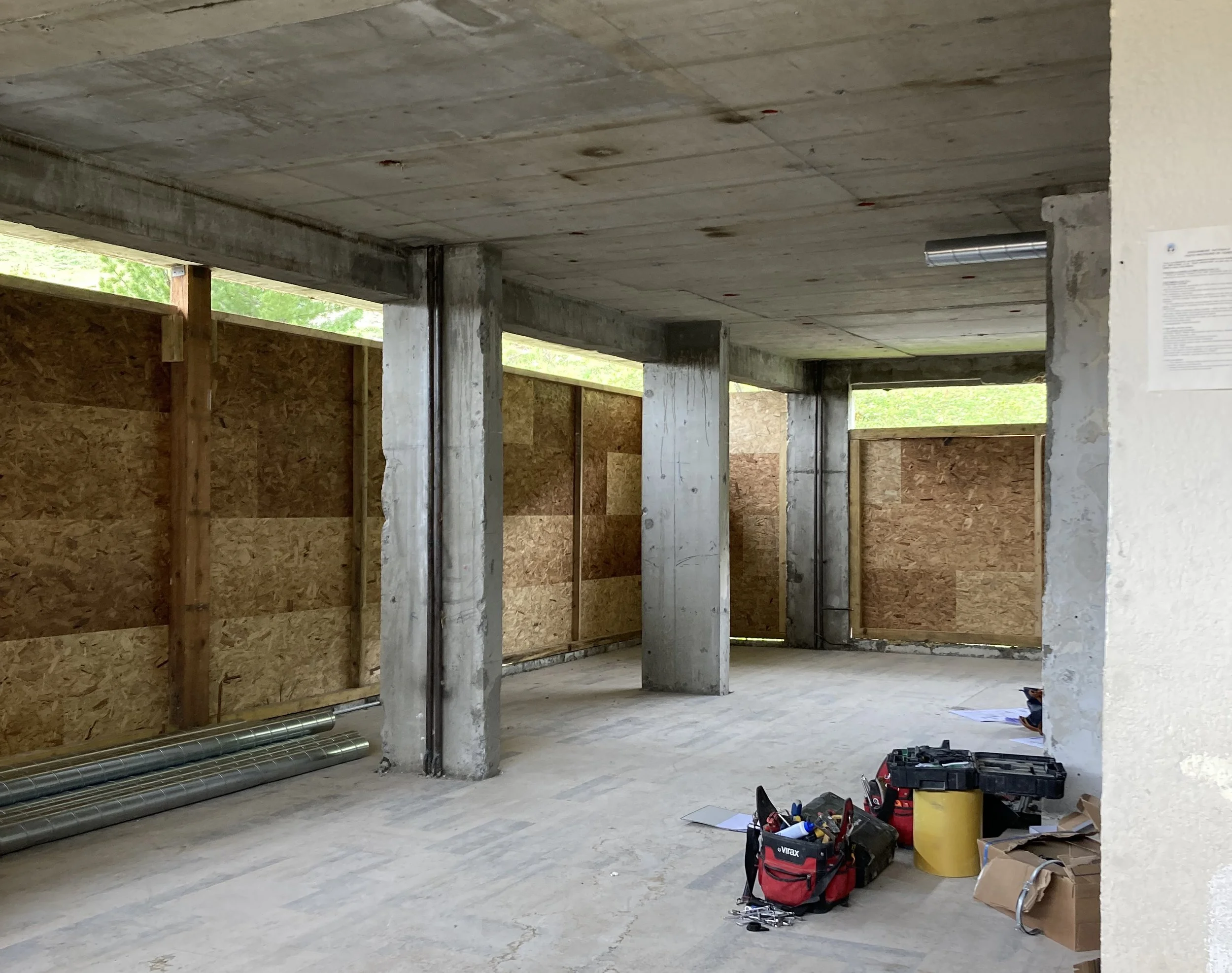 Intérieur d'une construction en cours avec des colonnes en béton et des murs en bois, outils et matériaux de construction sur le sol.