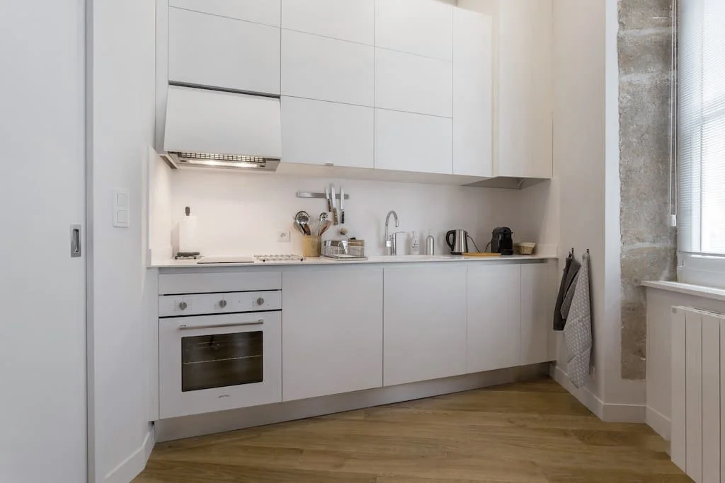 Cuisine moderne blanche avec des armoires hautes et basses, un évier, une plaque de cuisson, un four, et des appareils électroménagers sur le comptoir