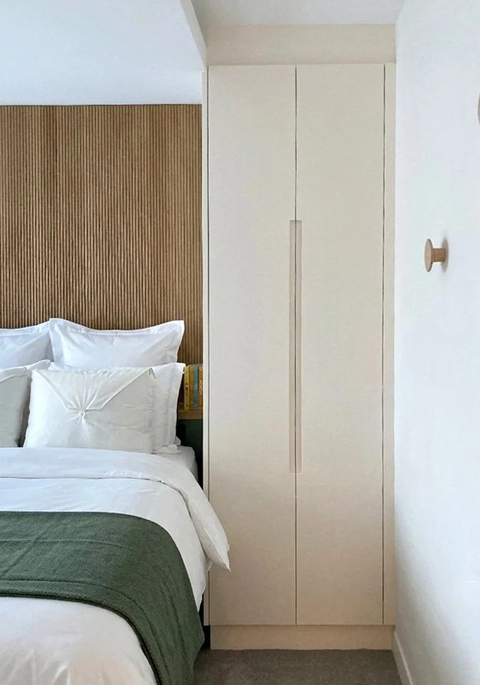 Coin chambre avec lit fait, présence d'une tête de lit en bois et d'une armoire blanche.