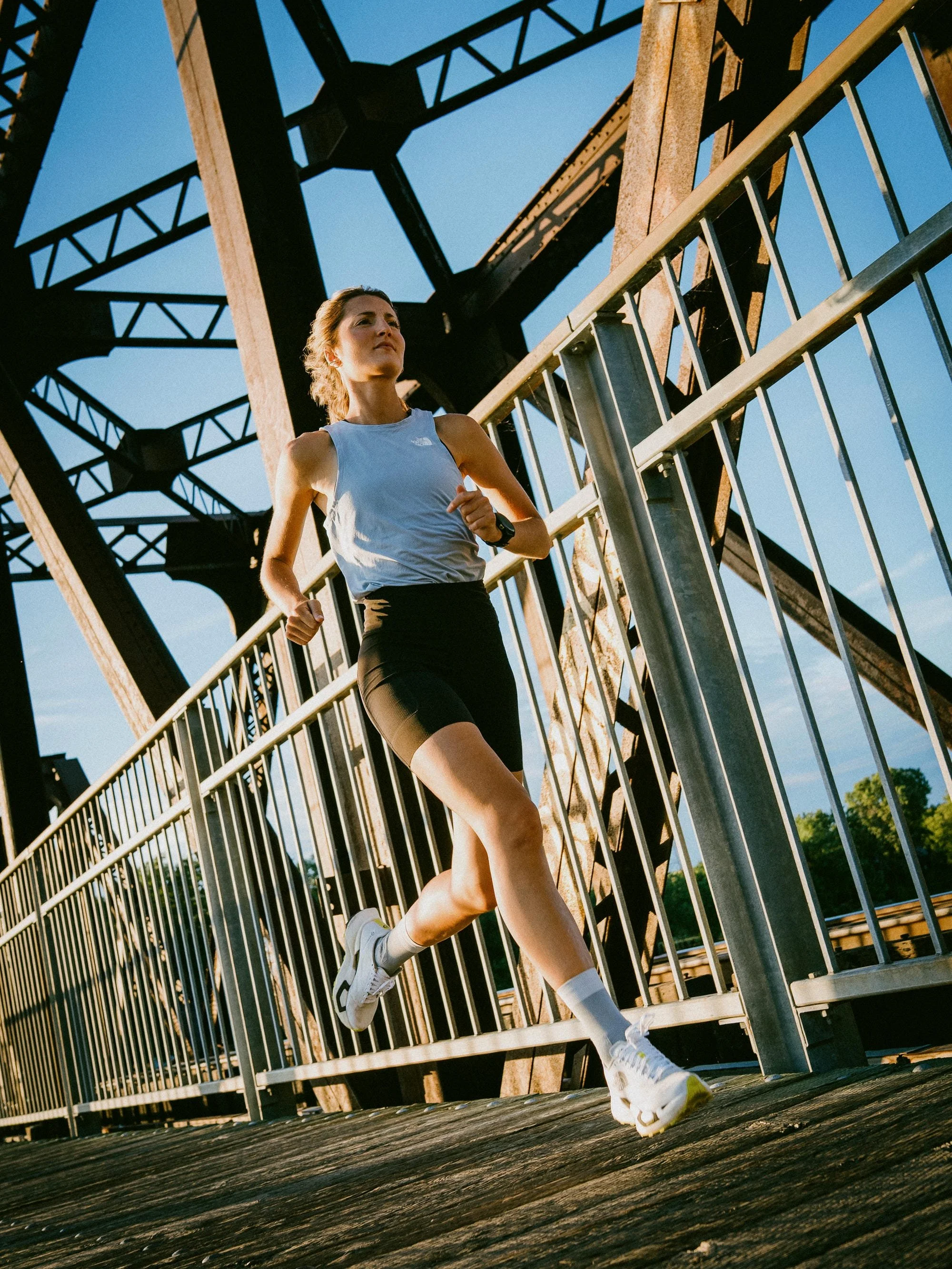 Une femme court sur une passerelle en métal sous un ciel bleu clair.