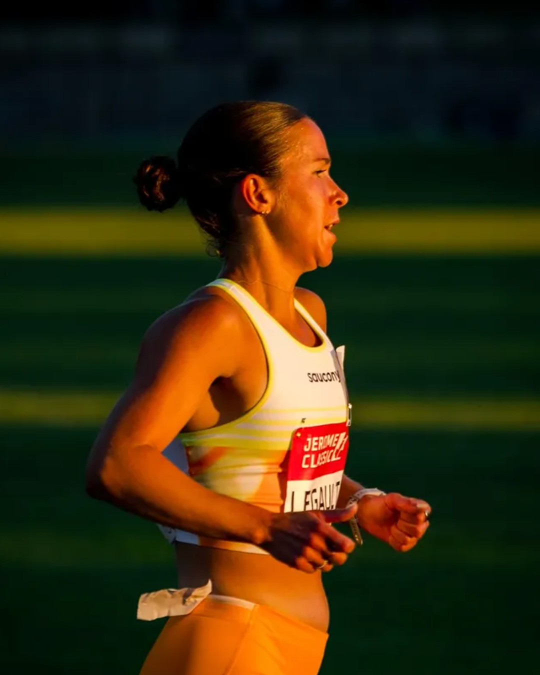 Une femme blonde en tenue de course, courant sur une piste lors d'une compétition, au coucher du soleil.