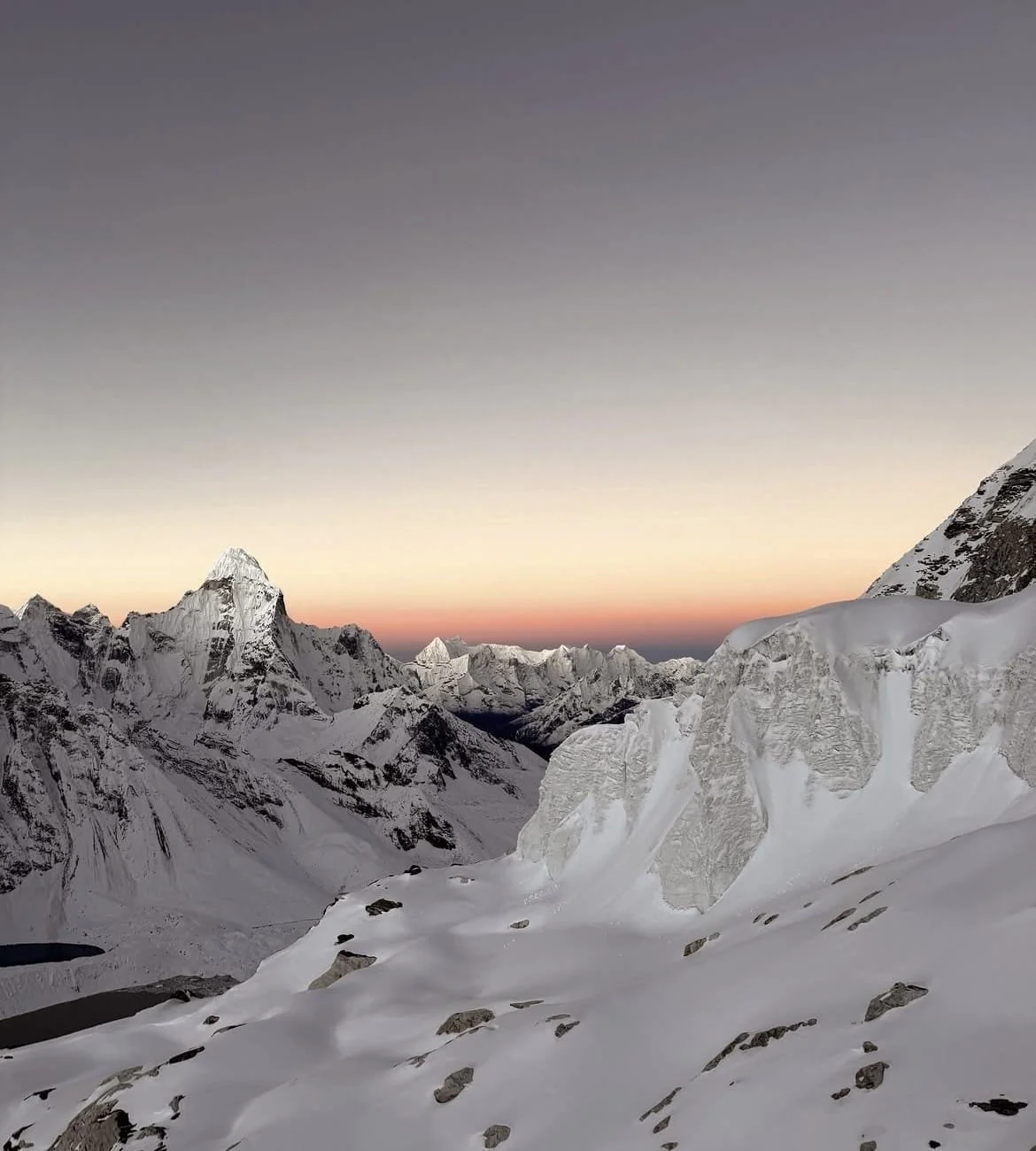 Montagnes enneigées au coucher du soleil, sommet impressionnant, ciel clair évoluant du gris au pastel