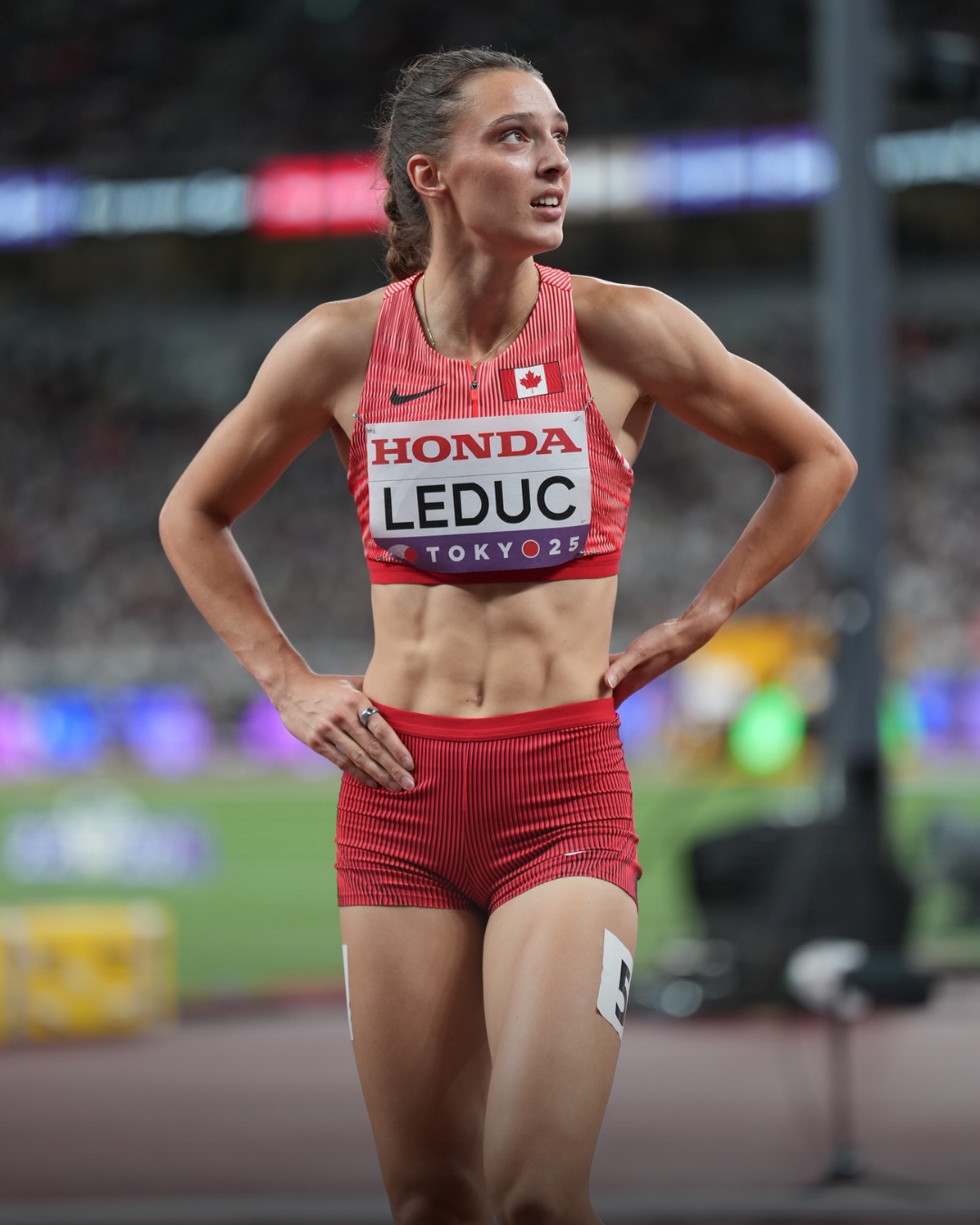 Une athlète féminine canadienne lors d'une compétition d'athlétisme, portant un uniforme rouge avec le nom Christiane Leduc et le drapeau canadien, en train de courir sur la piste de stade de Tokyo.