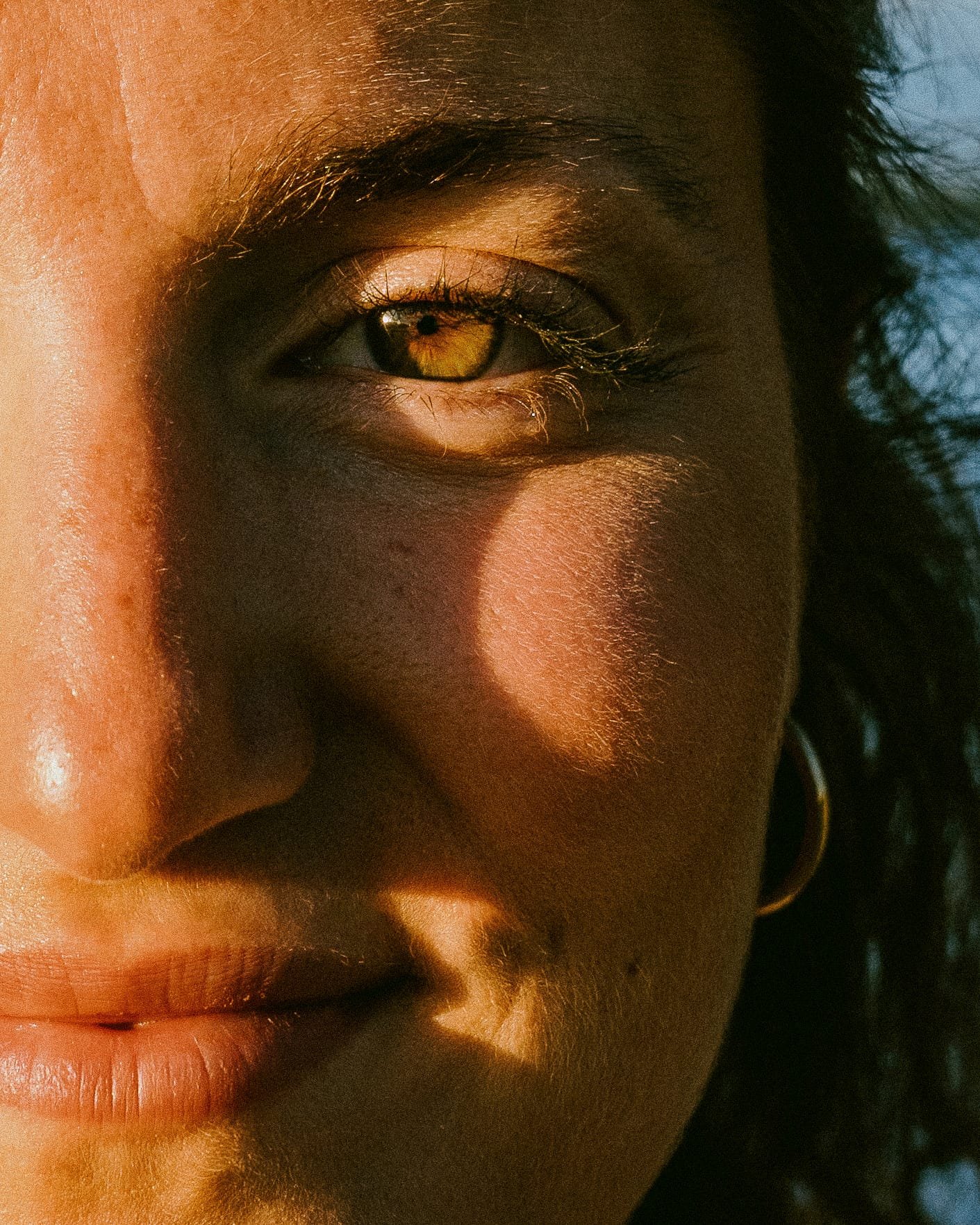Un gros plan d'œil d'une personne à la peau foncée, avec un iris doré et des cils longs, éclairé par une lumière douce et chaude.