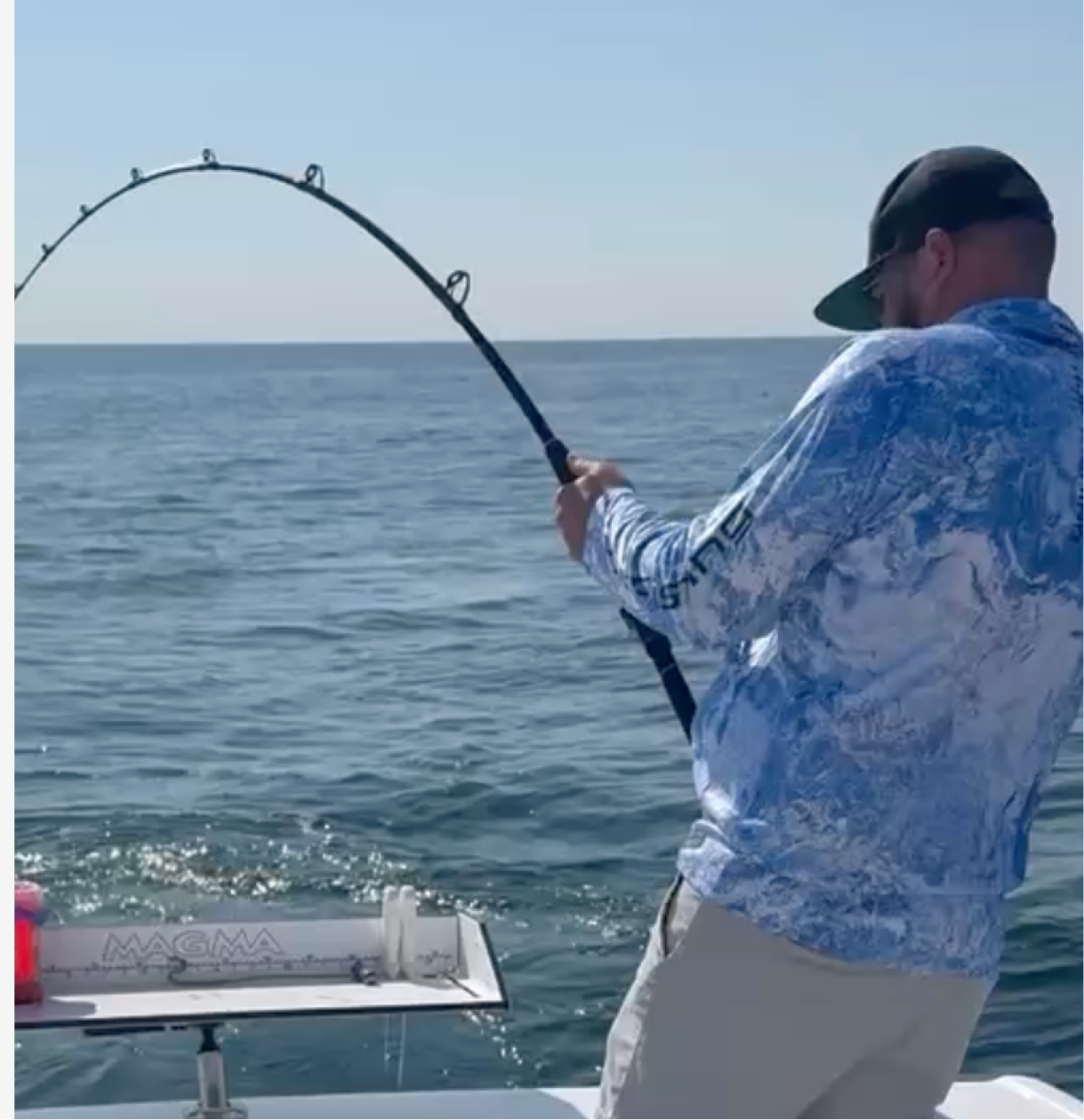 A man fishing on a boat in the ocean, holding a bent fishing rod.