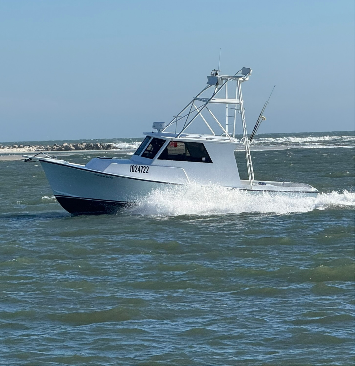 A white and black fishing boat moving through the water with waves splashing around it, clear blue sky in the background.