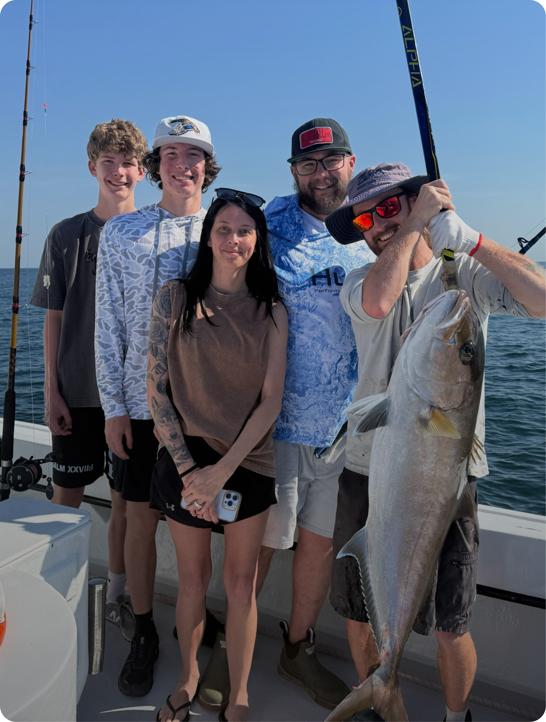 Group of six people on a boat with fishing rods, one person holding a large fish, on a sunny day at sea.